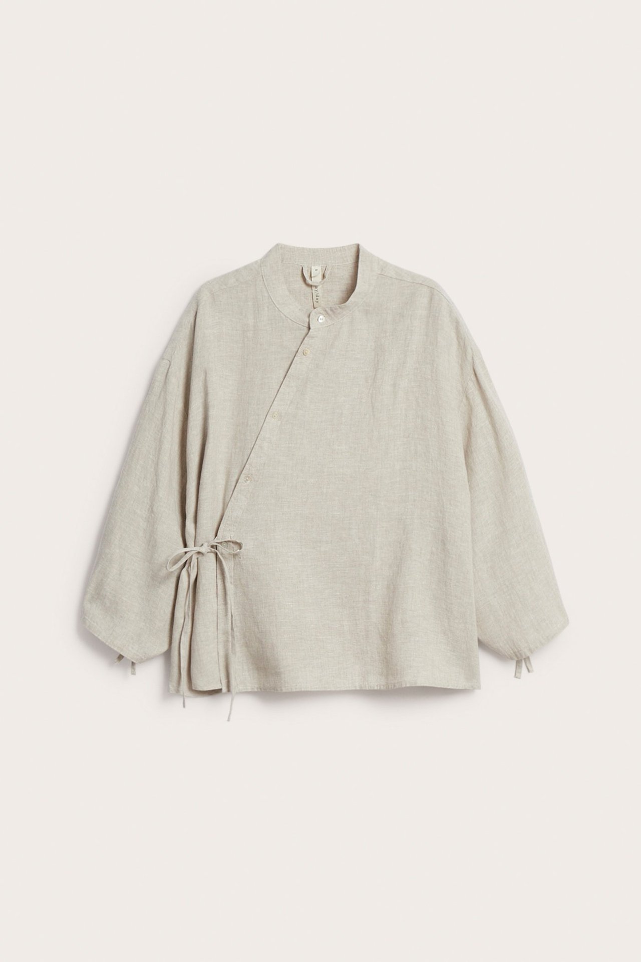 Widok z przodu beżowej lnianej bluzki z asymetrycznym zapięciem, wiązaniem w talii i stójką.