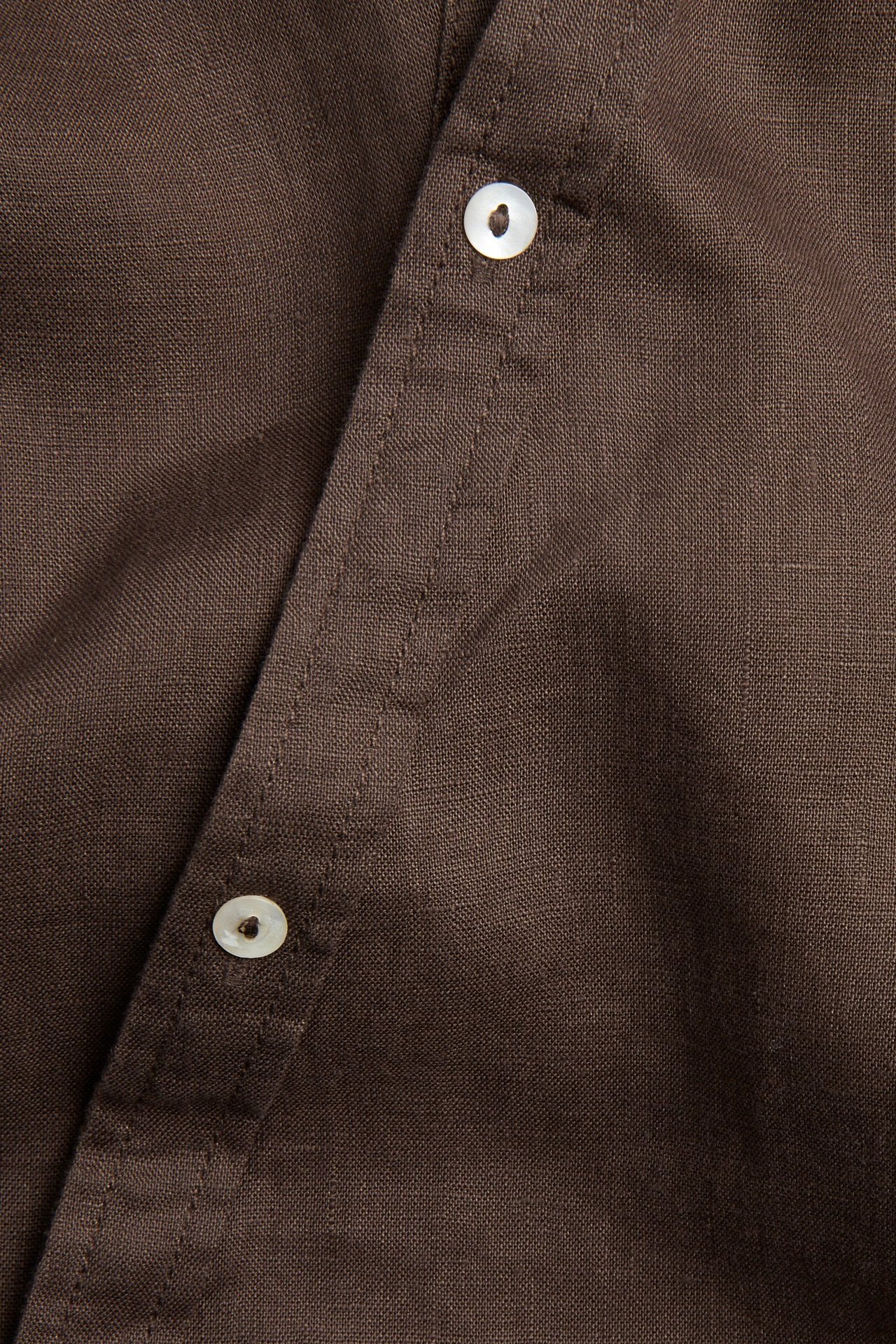 Lähikuva ruskeasta pellavapuseroista, jossa on vinottainen nappilista ja kaksi valkoista nappia.