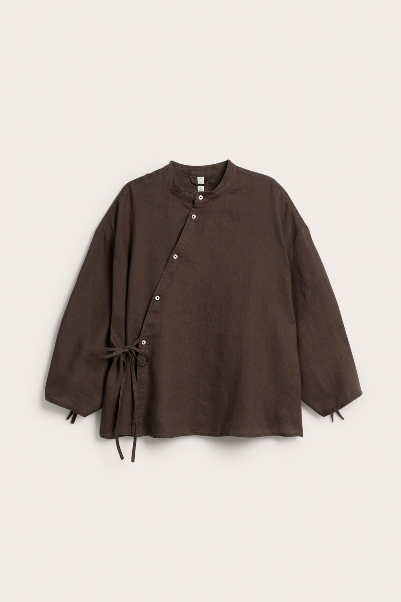 Widok z przodu brązowej lnianej bluzki ze stójką, ukośną listwą guzikową i wiązaniami po bokach.