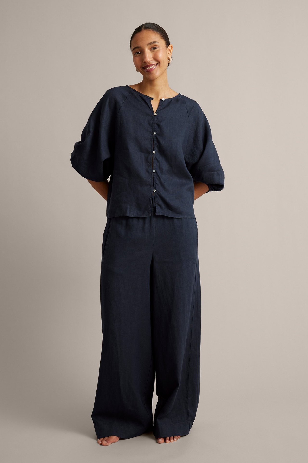 Z przodu: kobieta w granatowej lnianej bluzce z guzikami i pasujących szerokich spodniach.