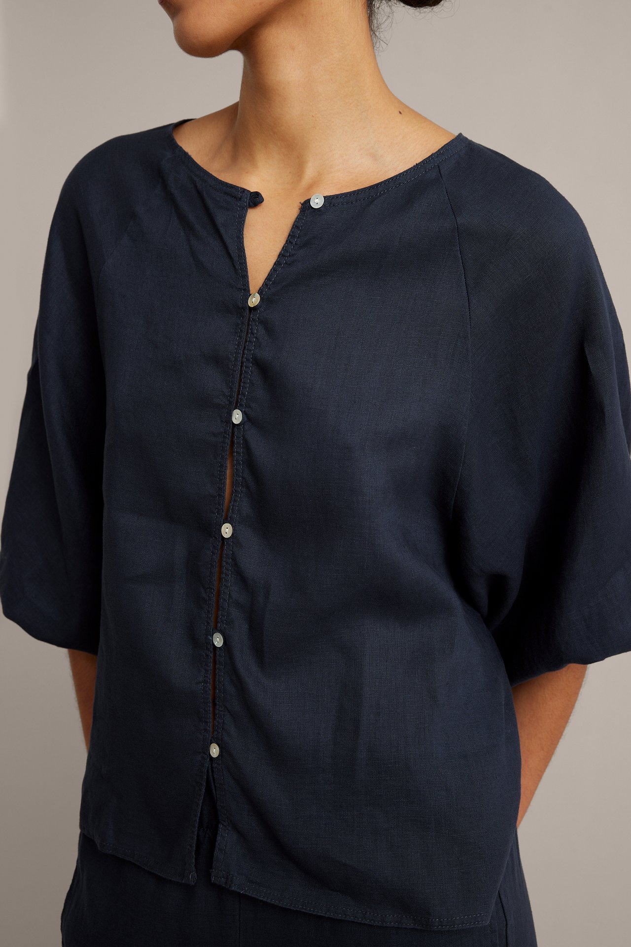 Widok z przodu: Kobieta w granatowej bluzce lnianej: okrągły dekolt, guziki, szerokie rękawy. Pasujące spodnie.