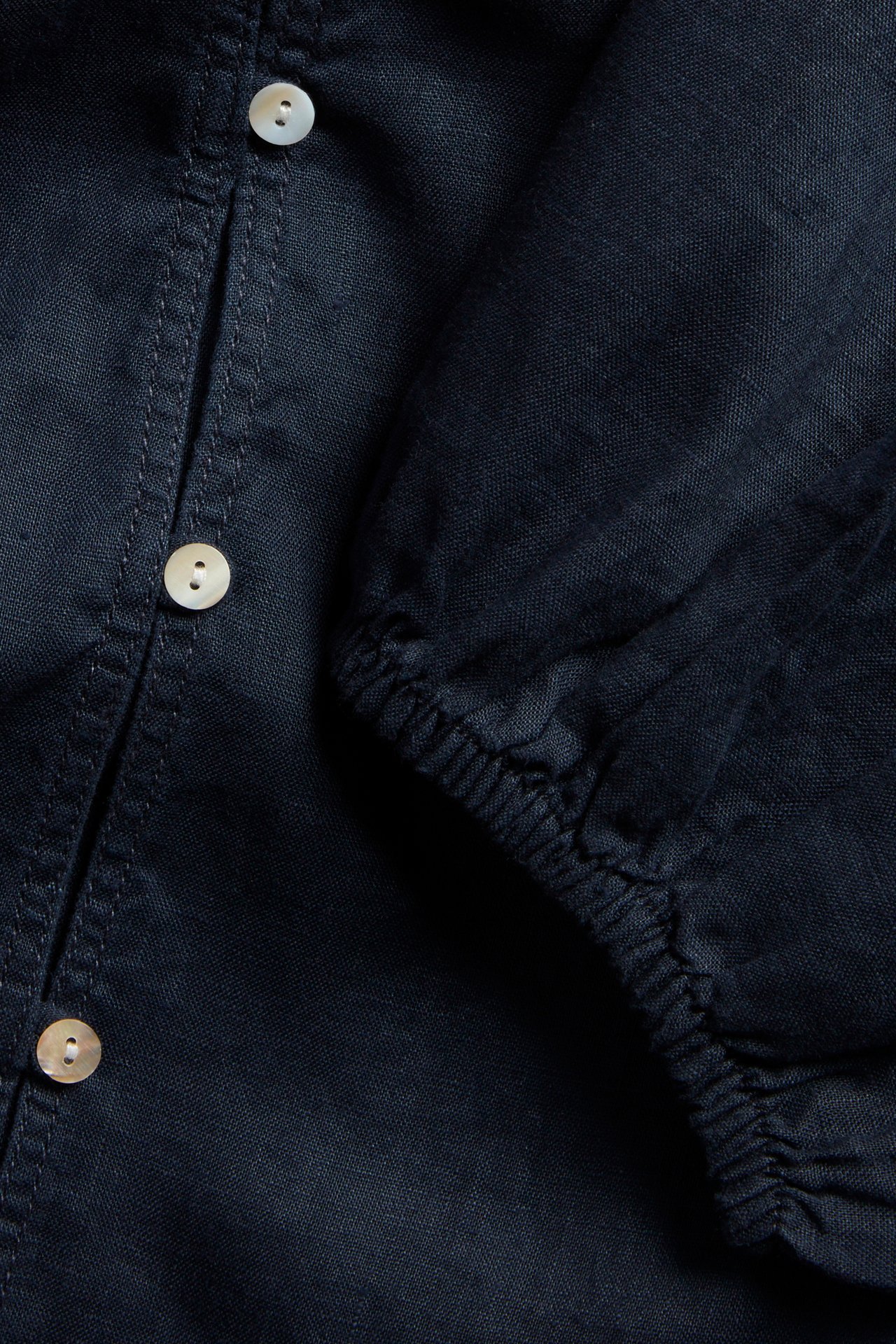 Zbliżenie ciemnoniebieskiej lnianej bluzki z jasnymi guzikami i elastycznym mankietem.