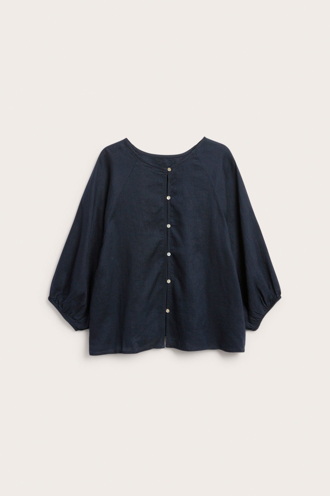 Ciemnoniebieska lniana bluzka, widok z tyłu, z okrągłym dekoltem, szerokimi rękawami raglanowymi, elastycznymi mankietami i guzikami.
