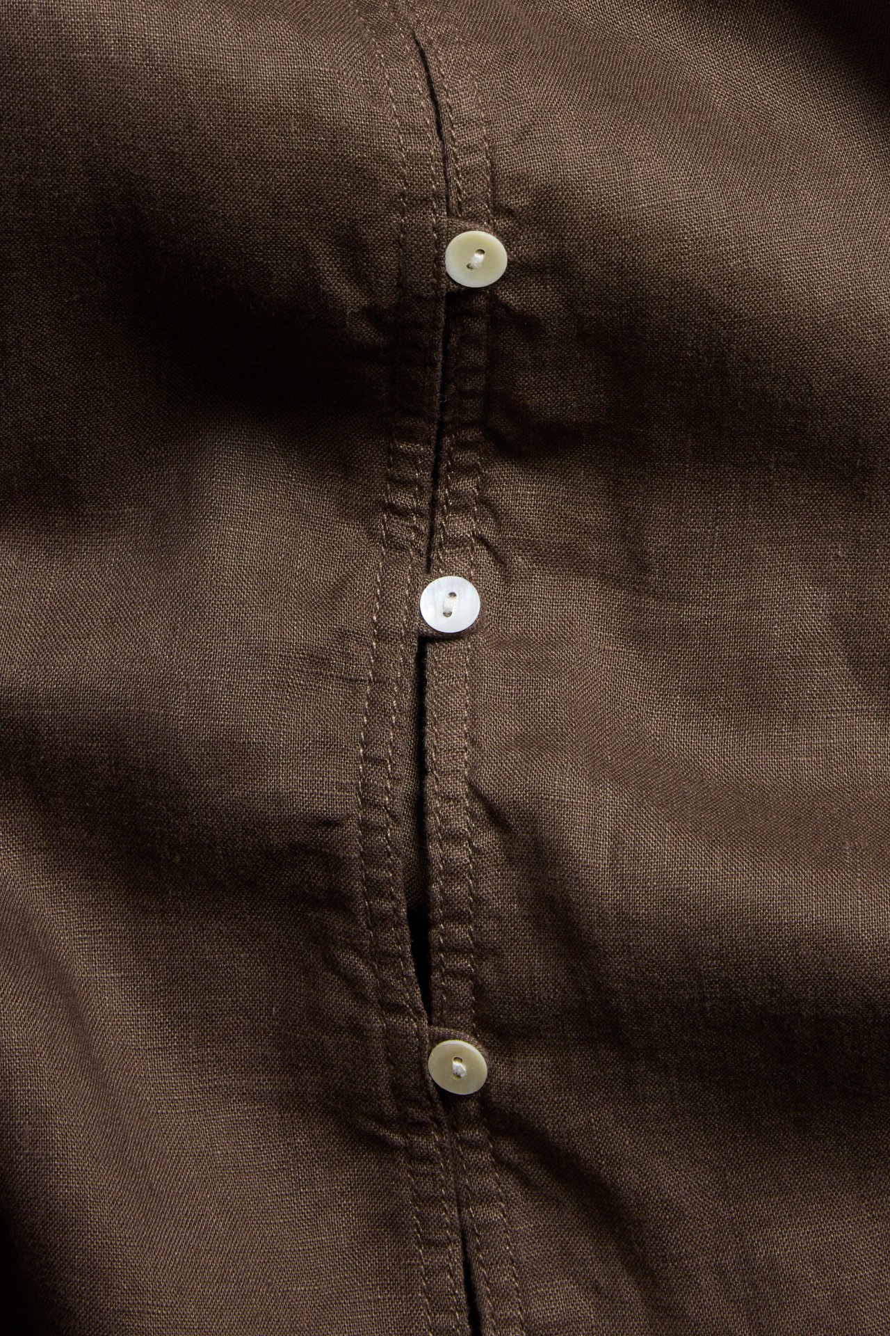 Zbliżenie brązowej lnianej bluzki z białymi guzikami na plisie guzikowej.