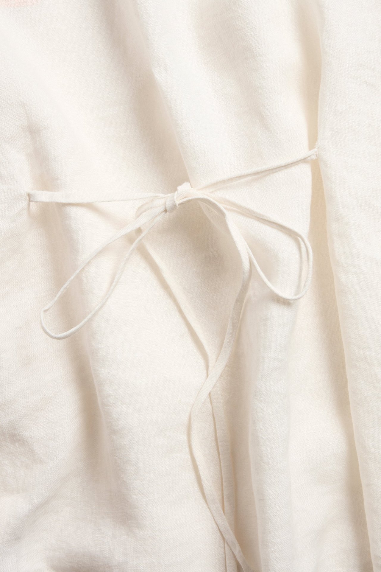 Zbliżenie na białą lnianą bluzkę z delikatnym wiązaniem zawiązanym w kokardę.