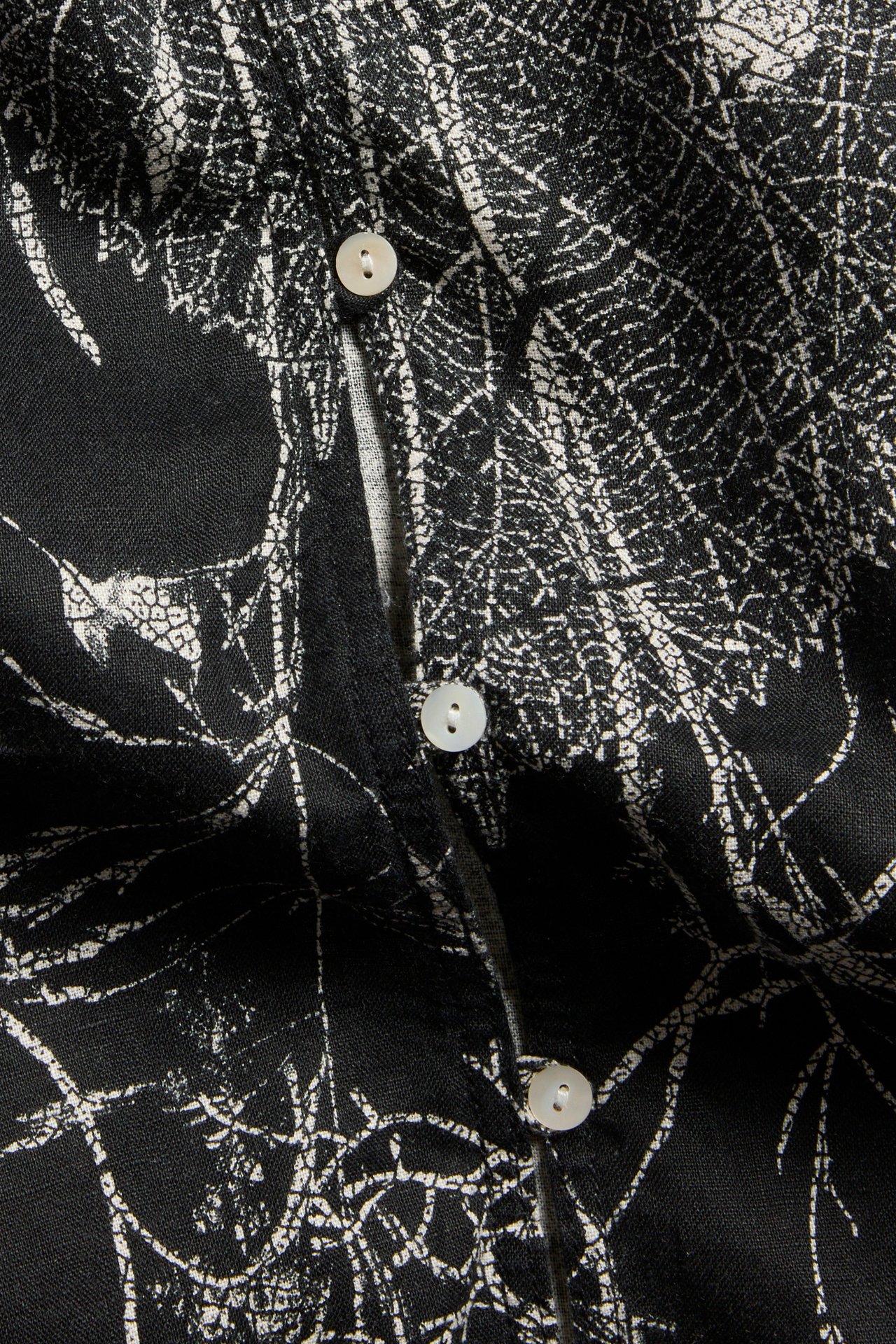 Zbliżenie czarnej lnianej bluzki z białym kwiatowym wzorem i białymi guzikami.