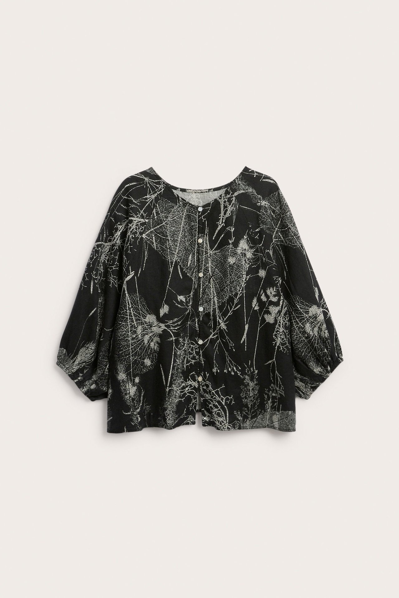 Widok z przodu czarnej lnianej bluzki w biały botaniczny wzór, z okrągłym dekoltem i guzikami.
