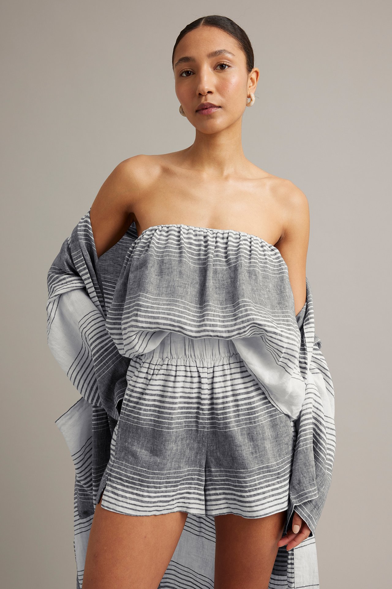 Edestäpäin nainen tummansinisissä, valkoraidallisissa pellavashortseissa, bandeau-topissa ja yhteensopivassa paidassa.