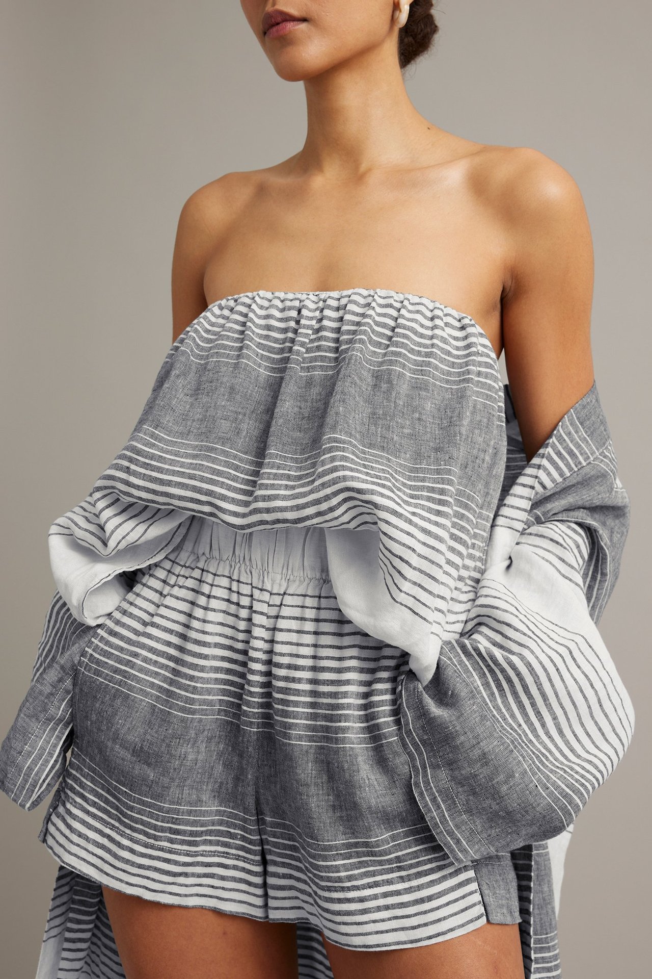Kobieta nosi granatowe lniane szorty w paski z gumką w pasie, pasujący top bez ramiączek i narzutkę.