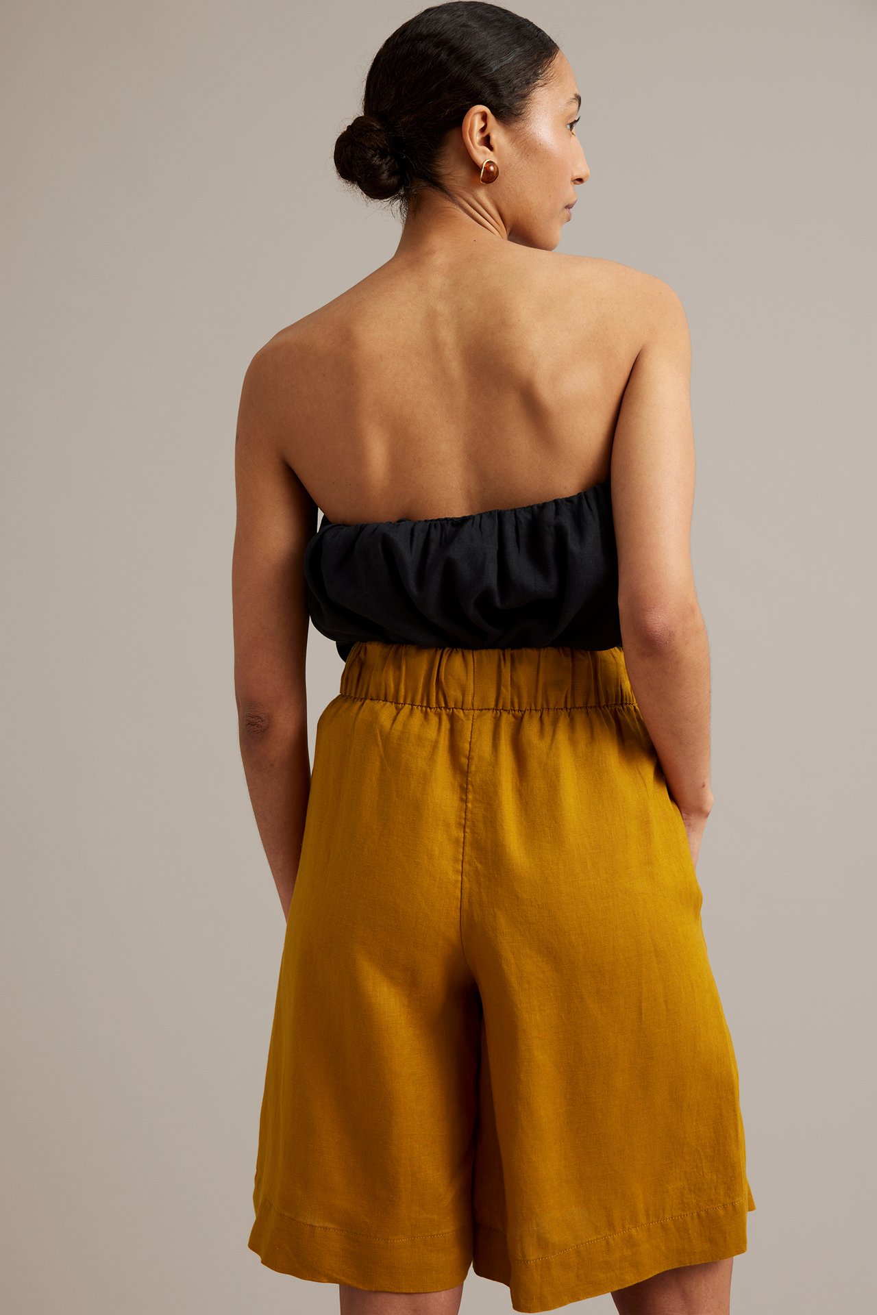 Kvinna bakifrån i gula knälånga linneshorts med resår i midjan och svart axelbandslös topp.