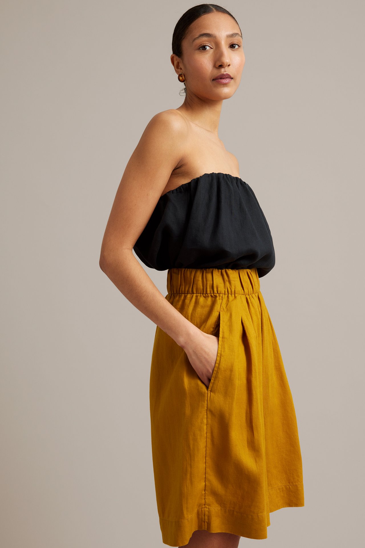 Sidovy av kvinna i gula knälånga linneshorts med resår i midjan och en svart axelbandslös topp.