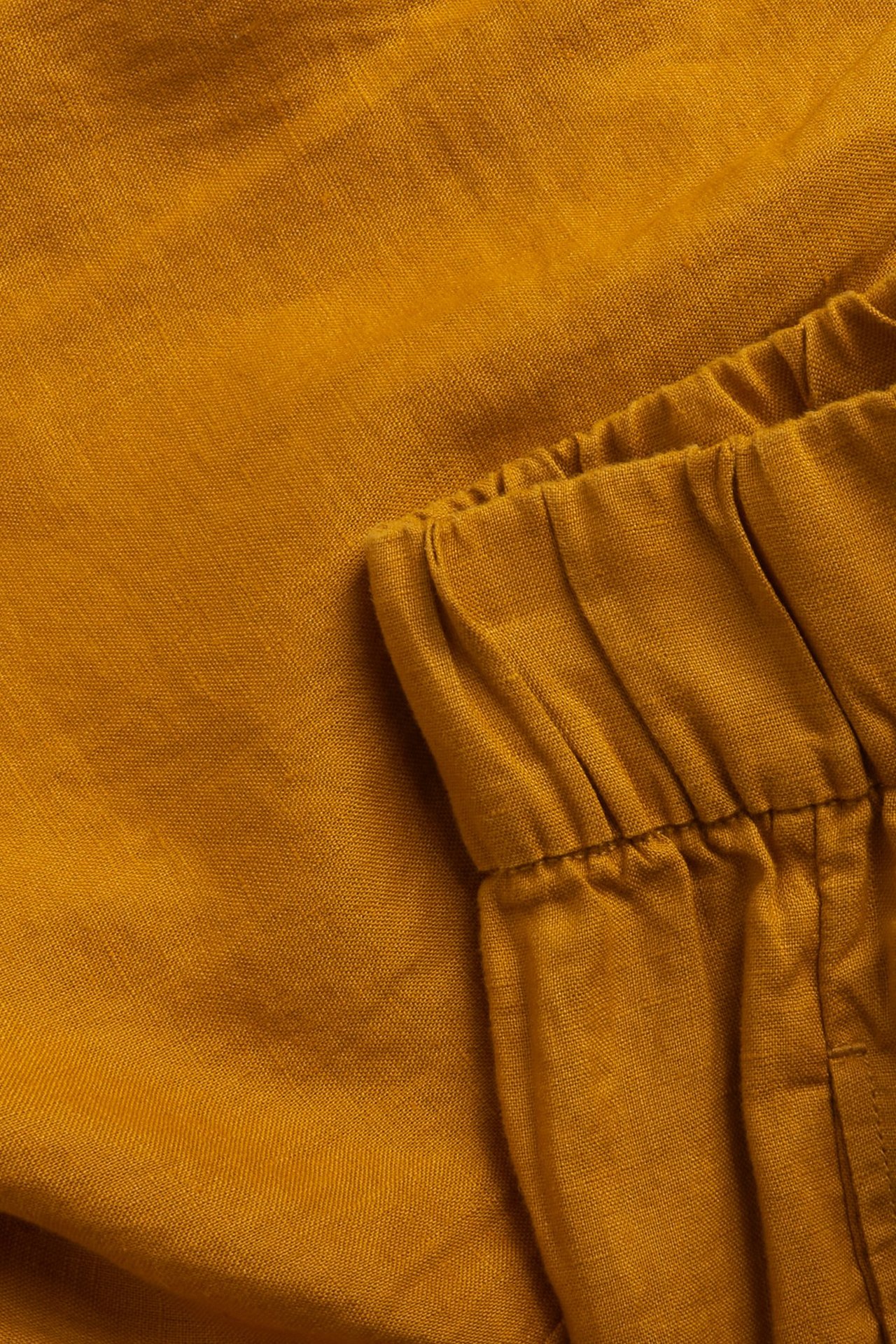 Zbliżenie na jednolite żółte lniane szorty z widocznym elastycznym pasem.