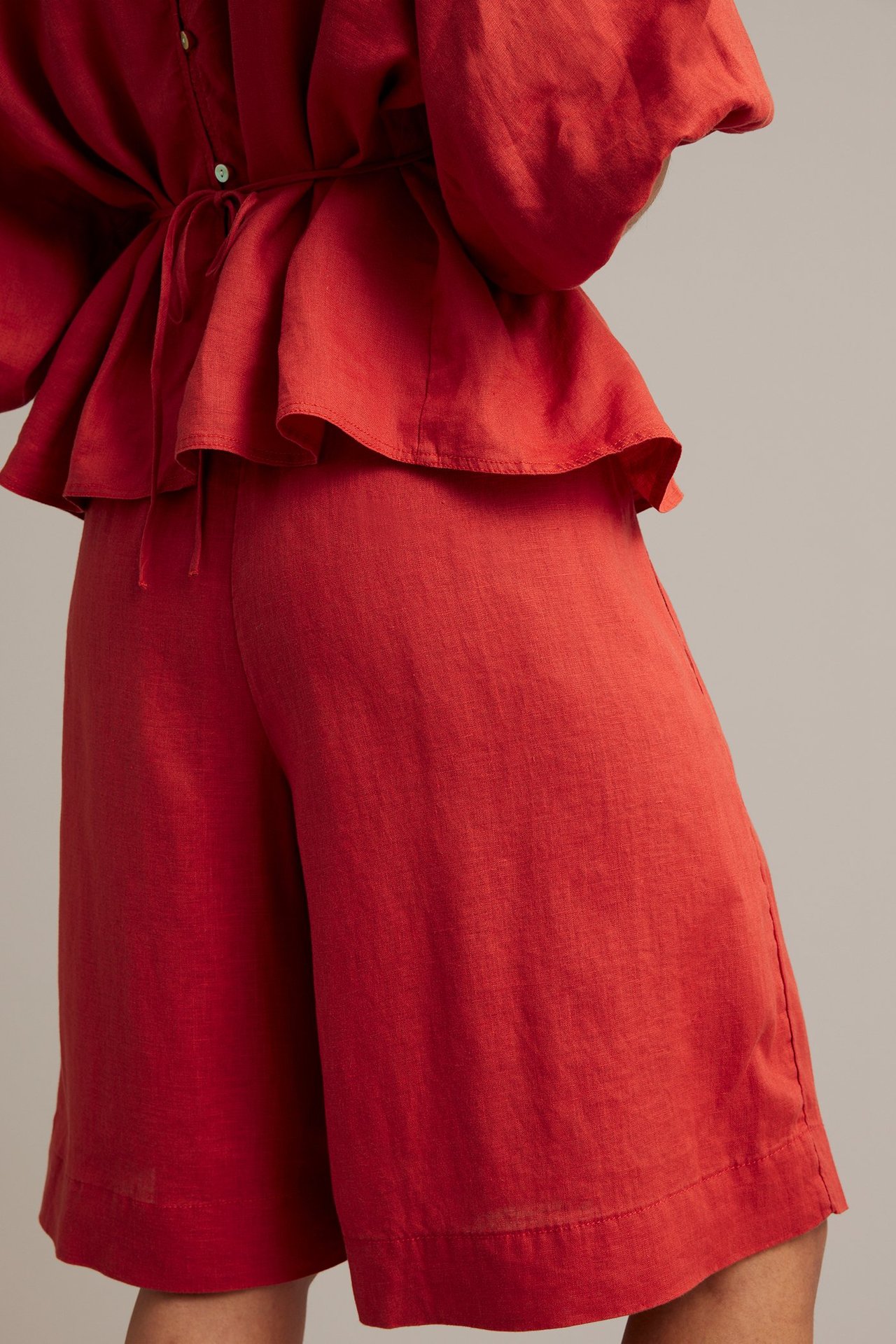 Bakifrån på kvinna i röda linnebermudashorts och matchande peplumtopp med knytband i midjan.