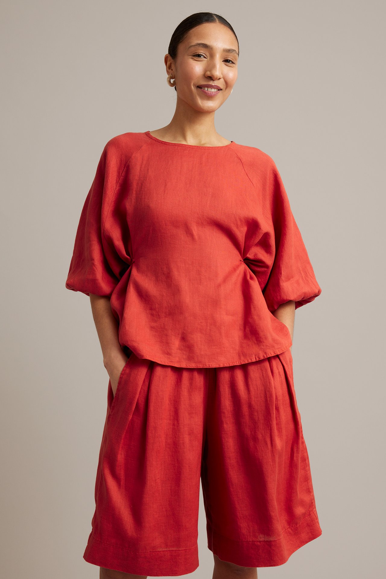 Frontvy: Kvinna bär röda knälånga linneshorts med resår i midjan och matchande röd linnetopp.