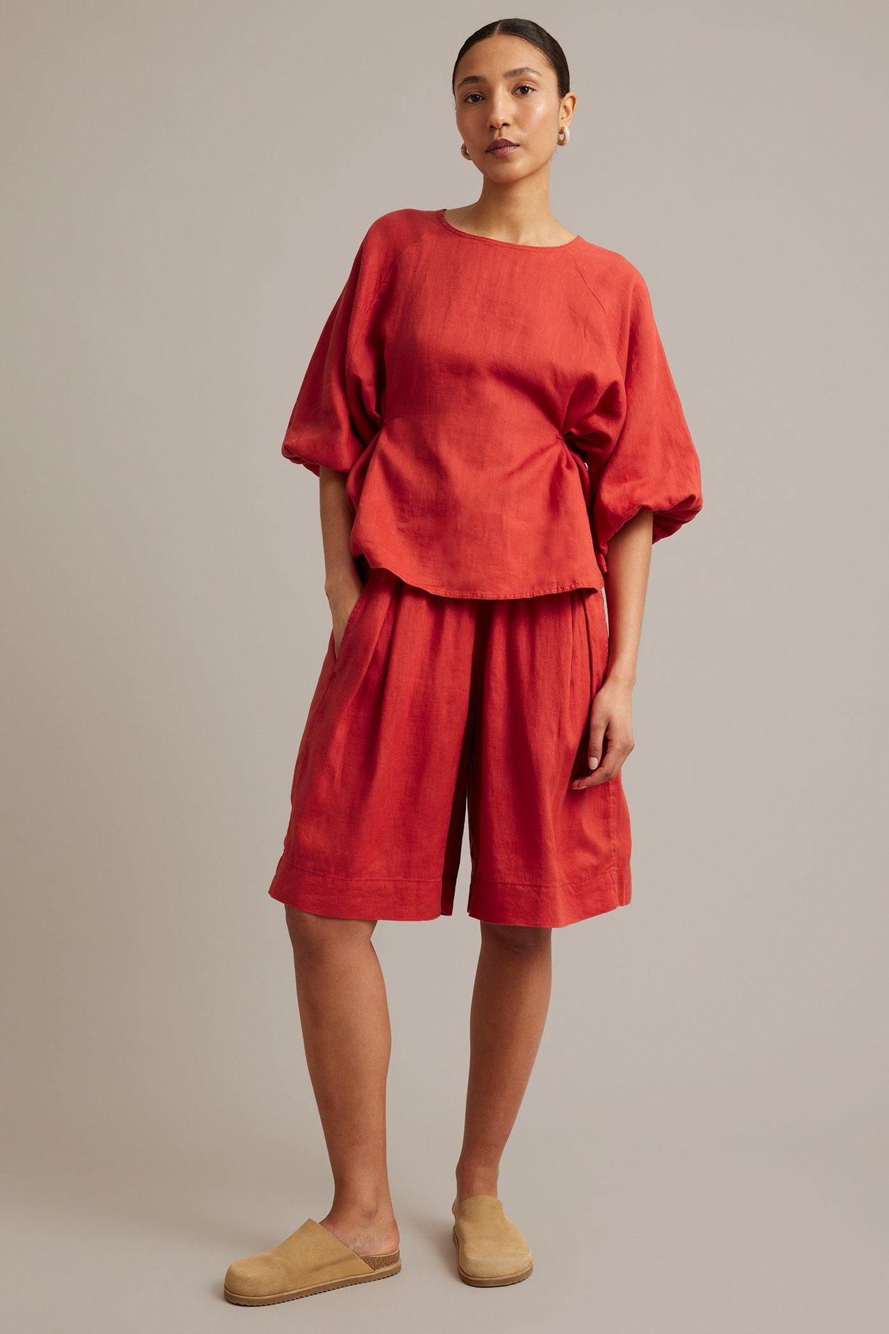 Framifrån, kvinna i röda knälånga linneshorts med resår i midjan och matchande röd linnetopp.