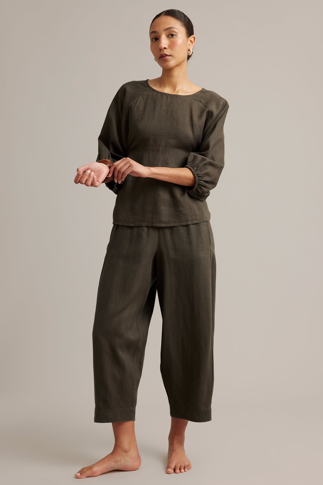 Nainen yllään tummanruskeat tynnyrijalkaiset pellavahousut ja yhteensopiva pellavatoppi, edestä.