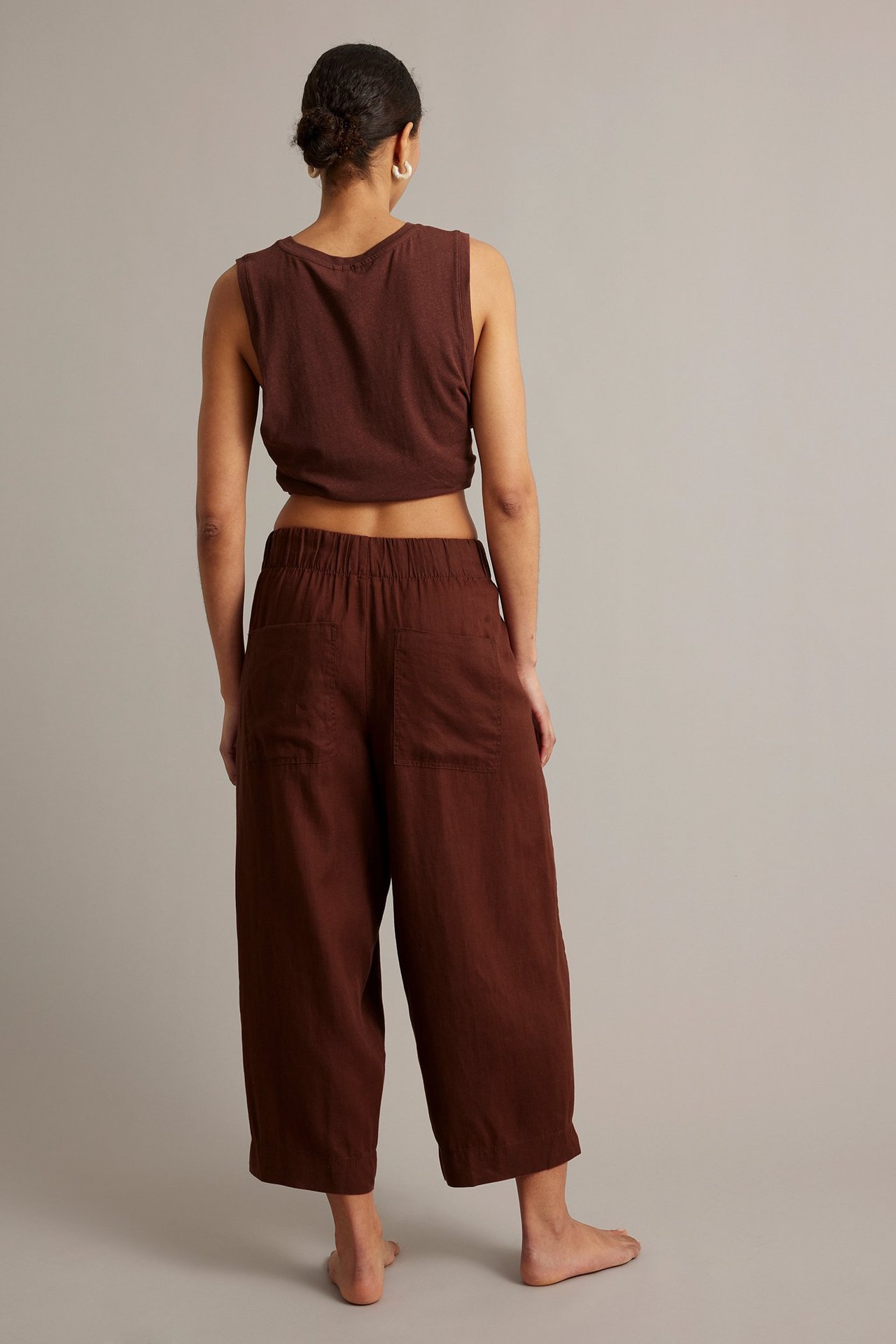 Widok z tyłu: kobieta w winnoczerwonych lnianych spodniach barrel-leg z tylnymi kieszeniami i pasującym crop topem.