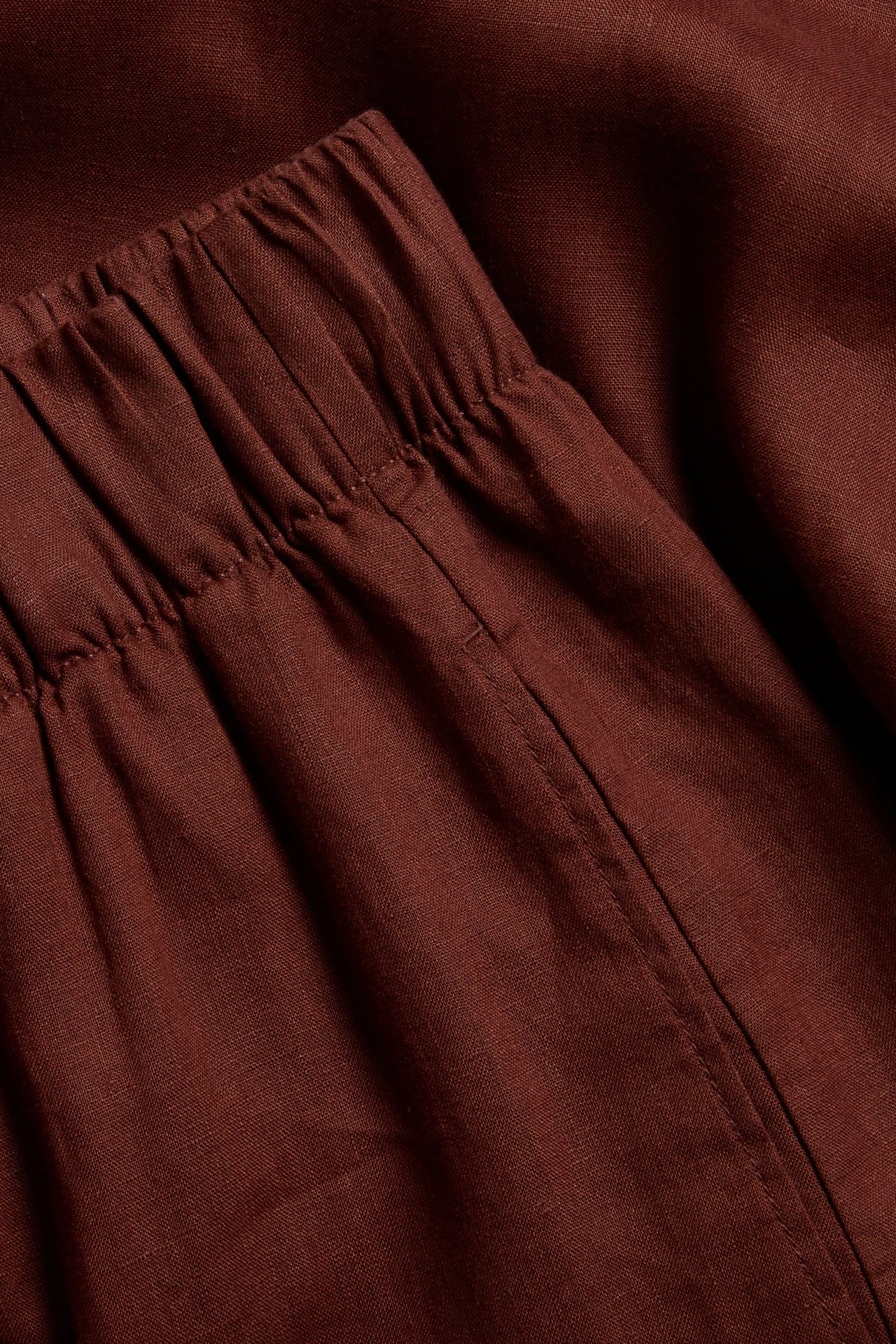 Zbliżenie na bordowe lniane spodnie z elastycznym pasem.