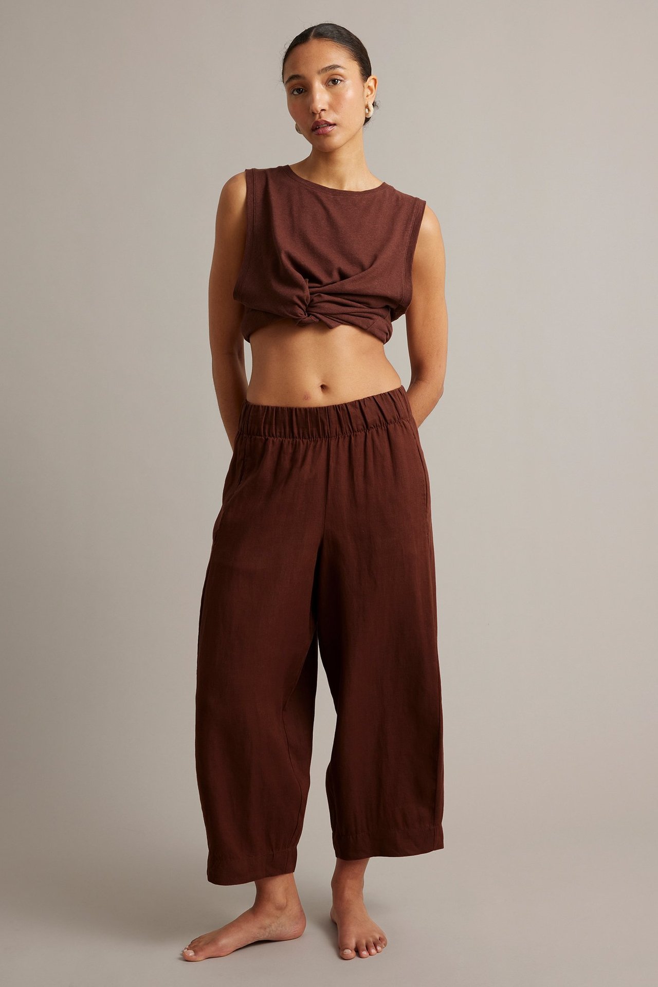 Widok z przodu: Kobieta w winnoczerwonych lnianych spodniach typu barrel-leg i pasującym, skręconym topie.