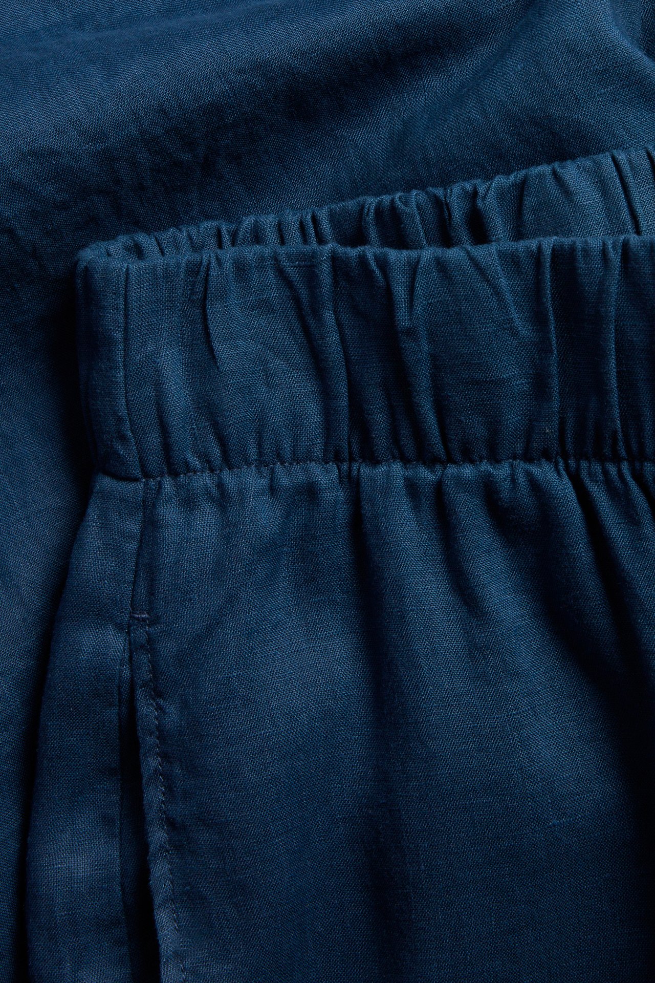 Zbliżenie na granatowe lniane spodnie z gumką w pasie.