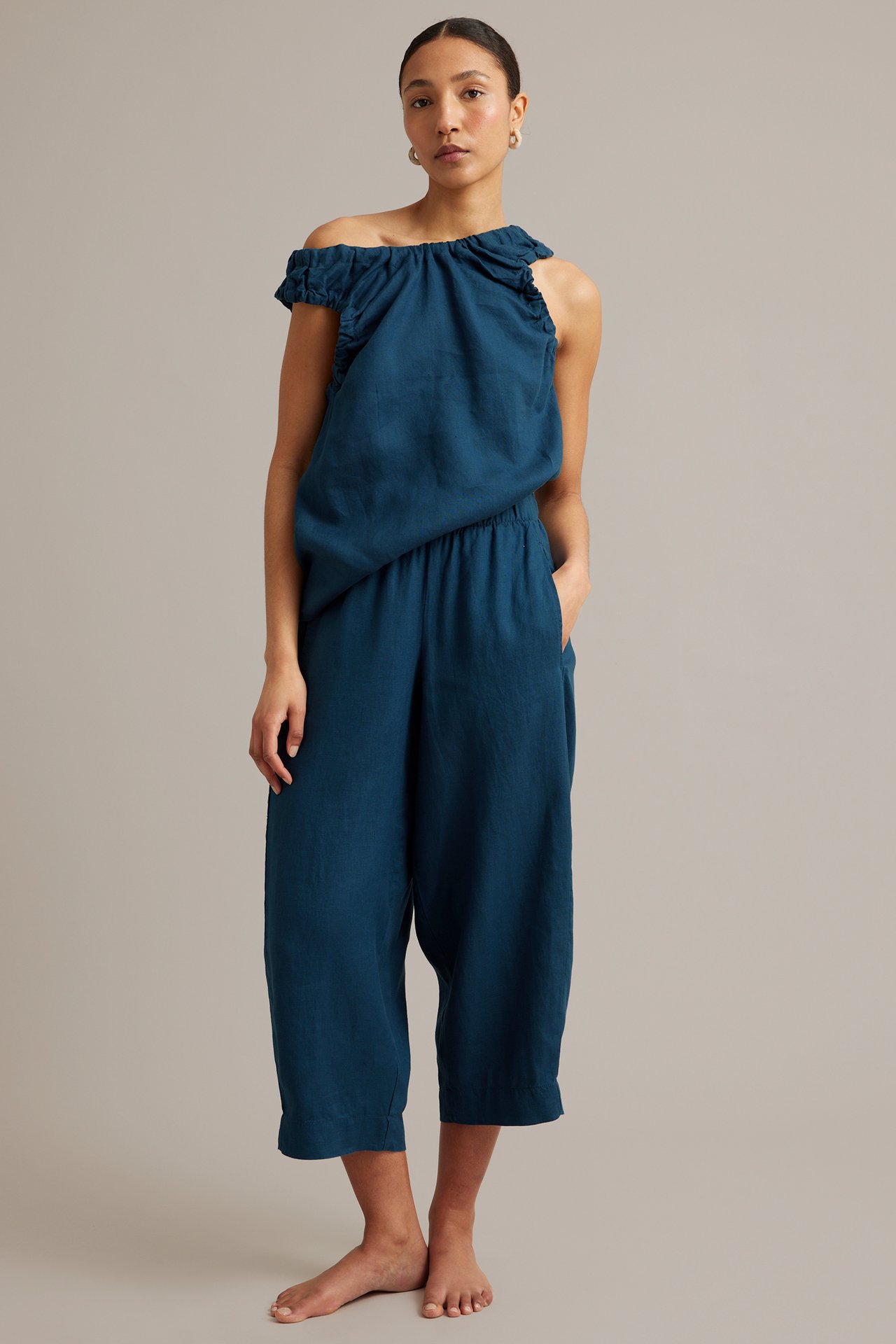 Framsida av kvinna i mörkblå linnebyxa med barrel fit, sidfickor och matchande off-shoulder topp.