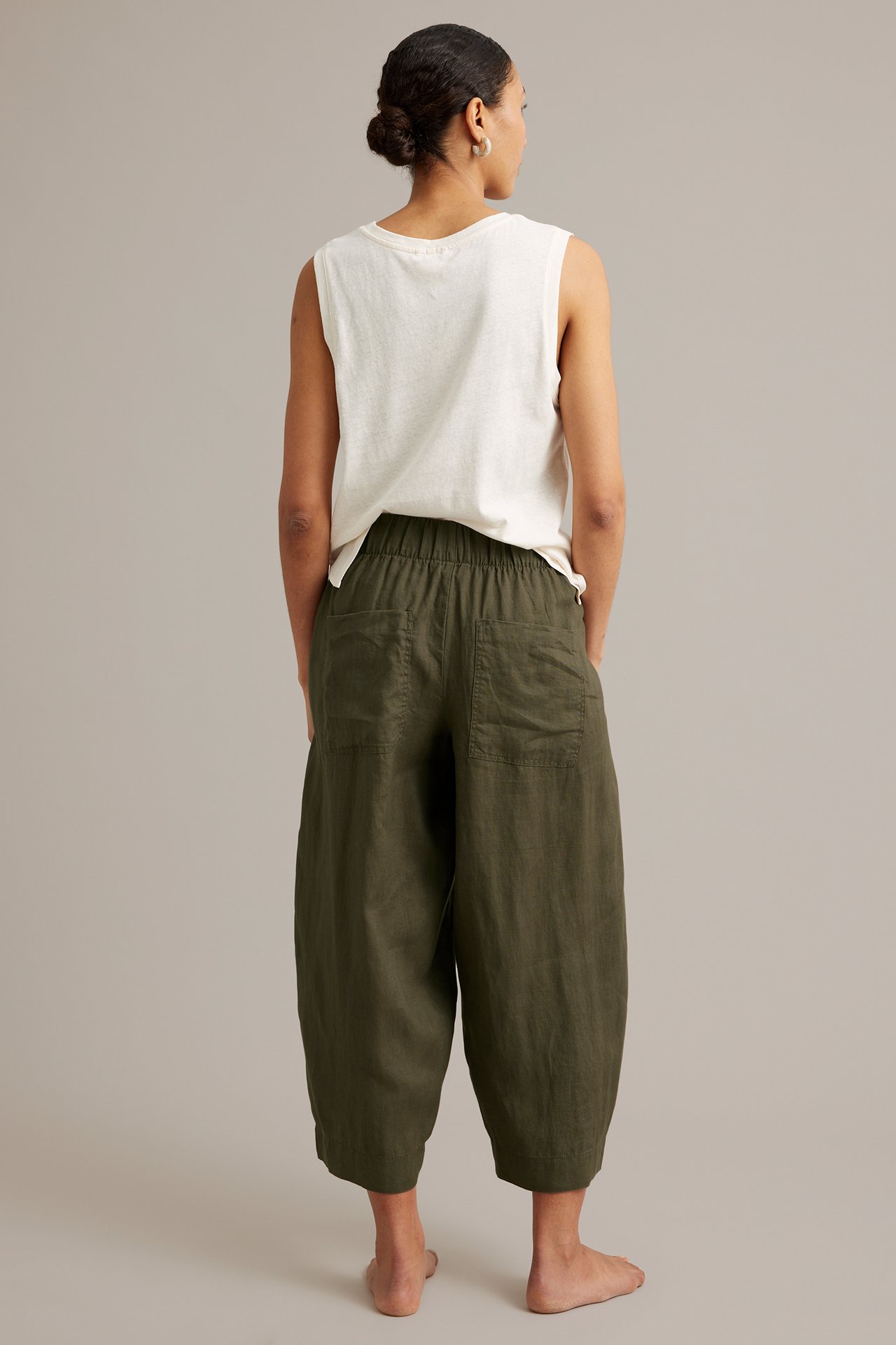 Takakuva: nainen yllään khakinvihreät pellavahousut joustovyötäröllä ja luonnonvalkoinen hihaton toppi.