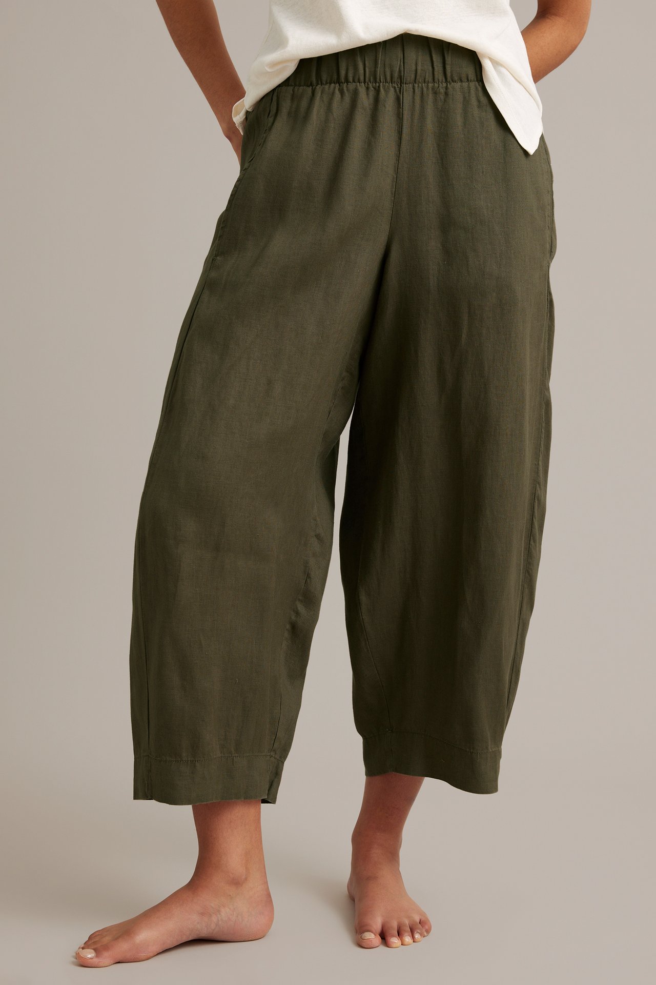 Kvinna bär khaki-gröna barrel leg linnebyxor med resår i midjan och vit t-shirt, framifrån.