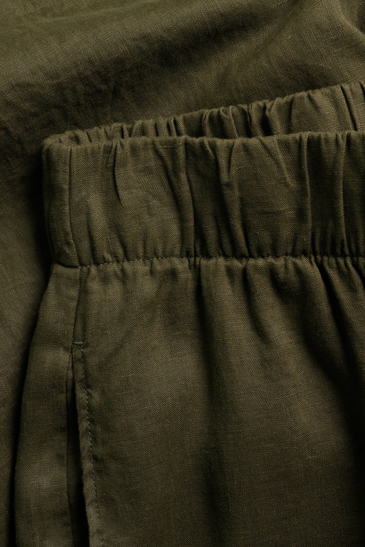 Zbliżenie na khaki zielone lniane spodnie z widoczną elastyczną talią.