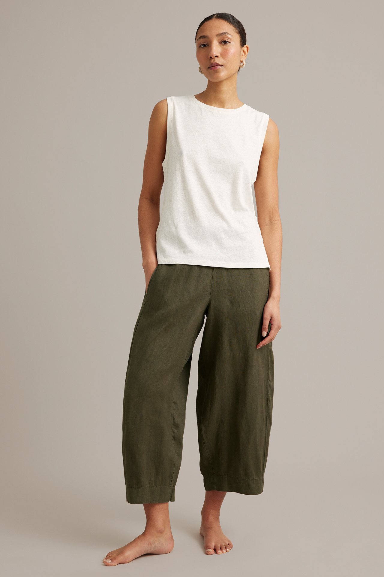 Framifrån: Kvinna i khakigröna linnebyxor med barrel-fit och resår samt vit ärmlös topp.