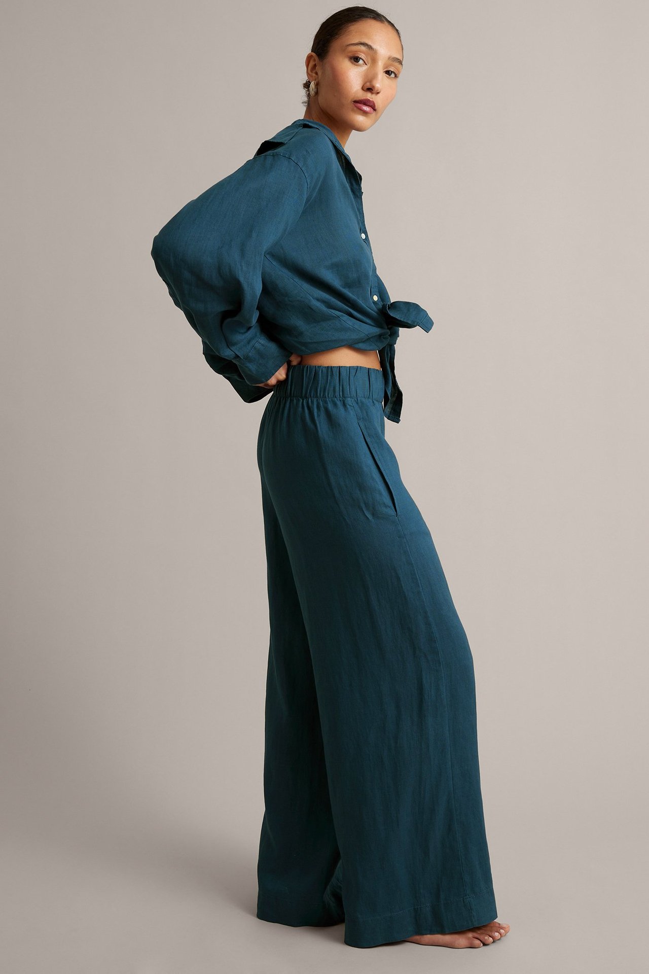 Nainen tummansinisissä leveissä pellavahousuissa, joissa joustava vyötärö, ja yhteensopivassa solmitussa paidassa.