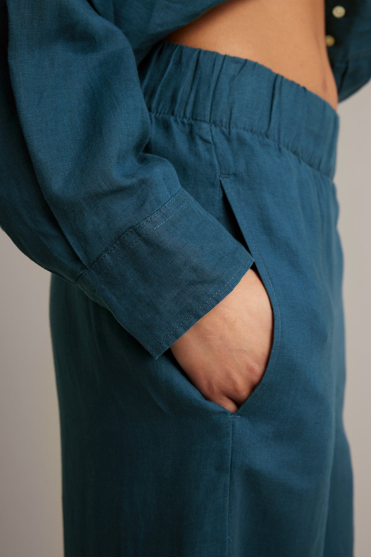 Närbild, sidovy av kvinnas hand i fickan på blå vida linnebyxor och matchande skjorta.