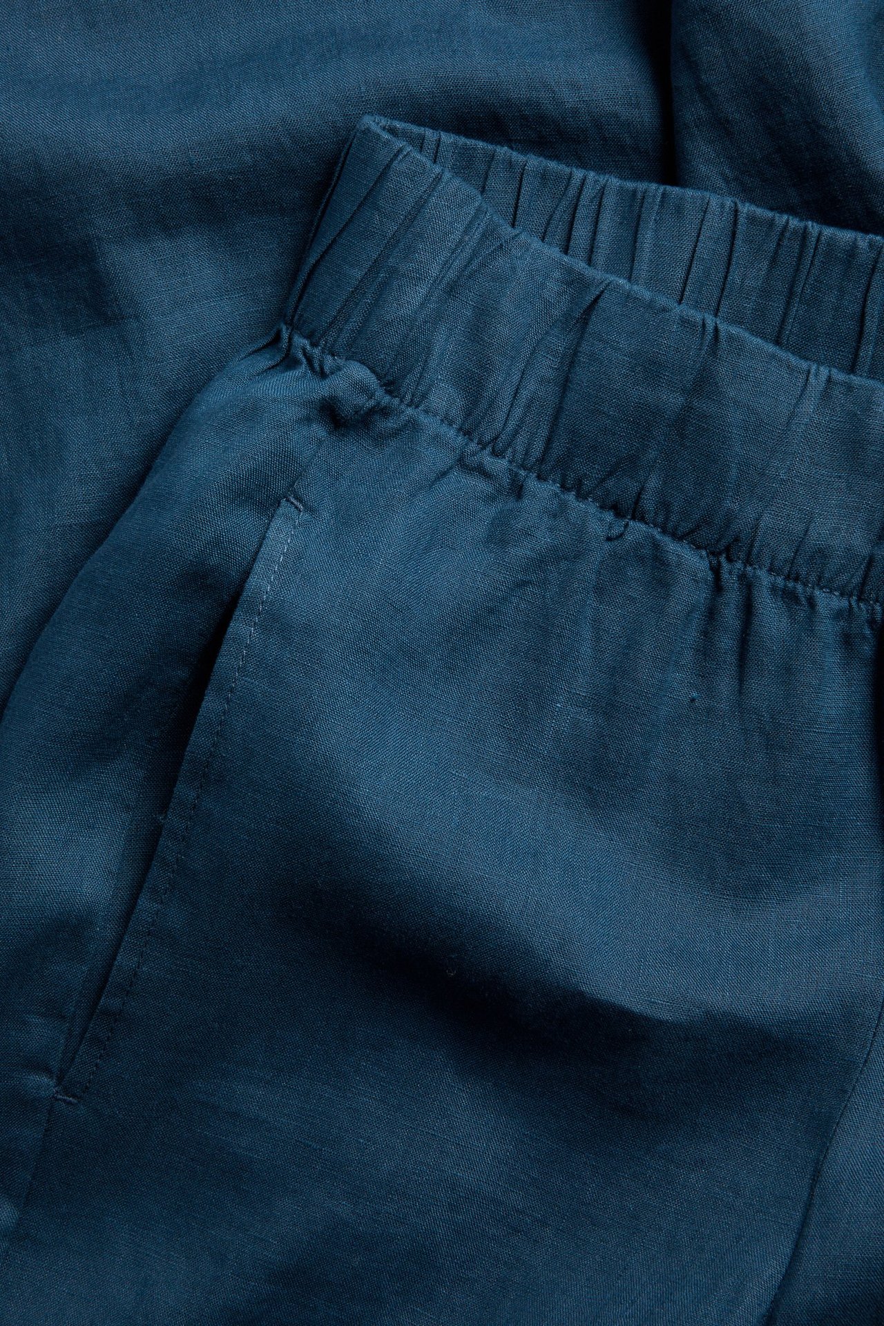 Nærbilde av blå linbukse med strikk i midjen og sidelomme.