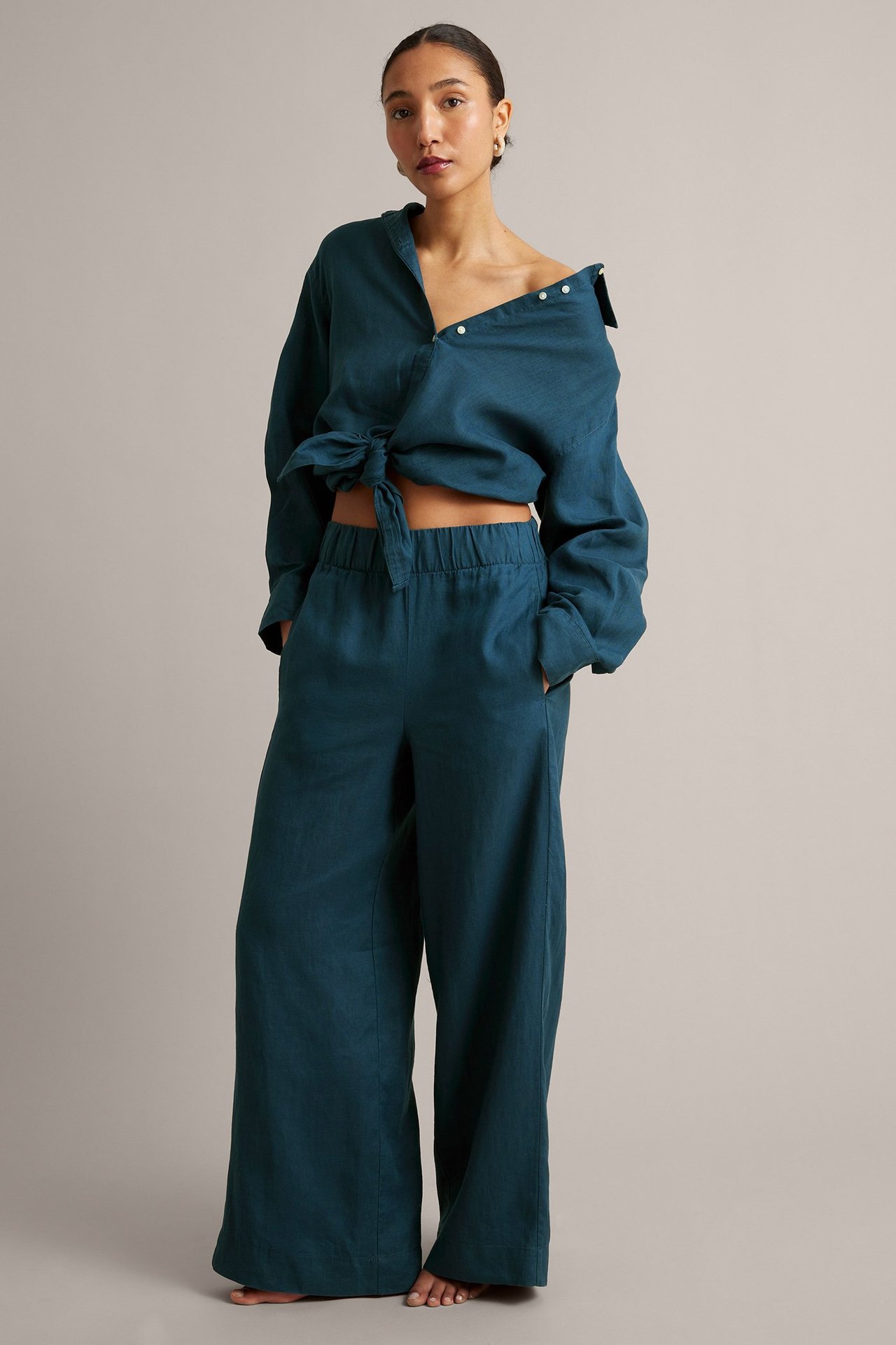 Edestäpäin: nainen sinisissä leveälahkeisissa pellavahousuissa joustovyötäröllä ja solmitussa pellavapaidassa.