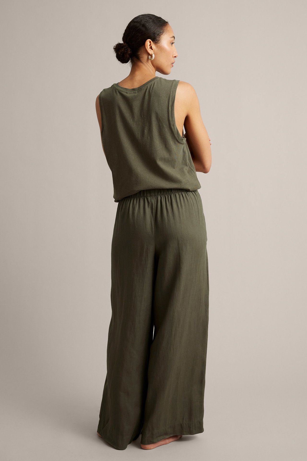 Widok z tyłu kobiety w oliwkowych, szerokich lnianych spodniach z elastyczną talią i pasującym topie bez rękawów.