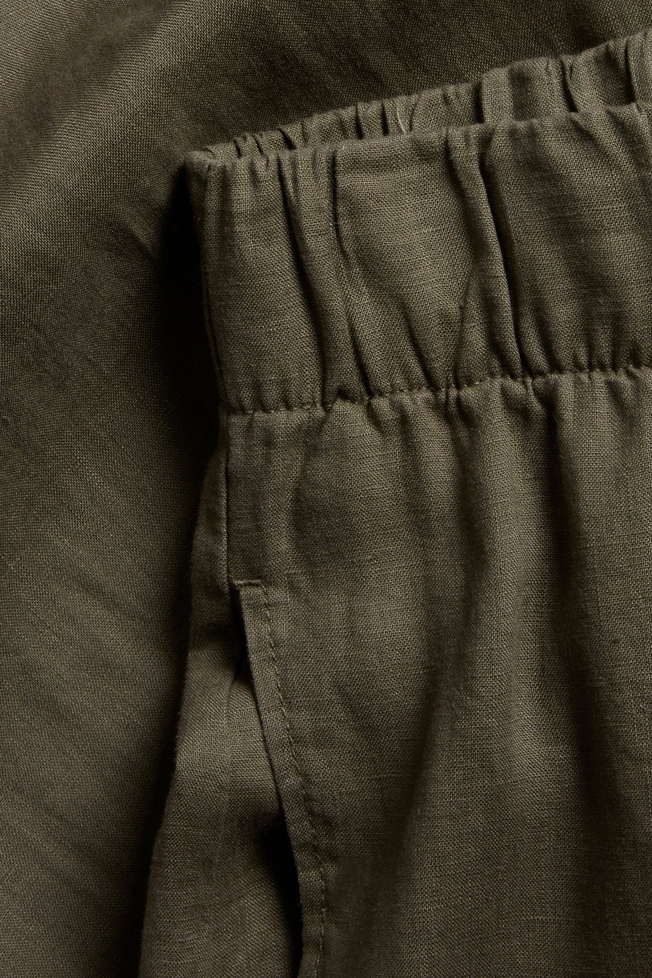 Zbliżenie na khaki zielone lniane spodnie z elastyczną talią i boczną kieszenią.