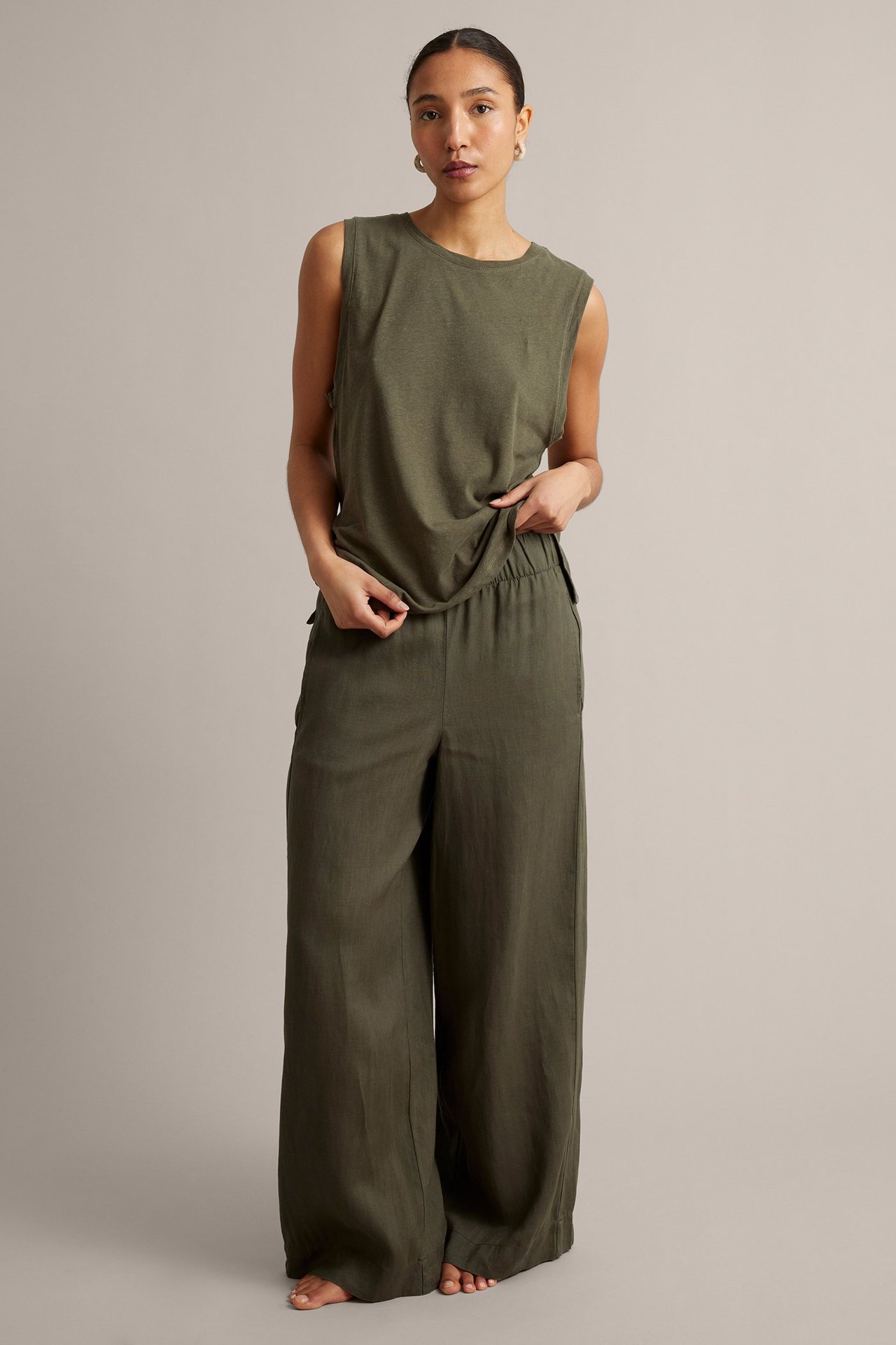 Widok z przodu: kobieta w szerokich, lnianych spodniach khaki z gumką w pasie i pasującym topie bez rękawów.