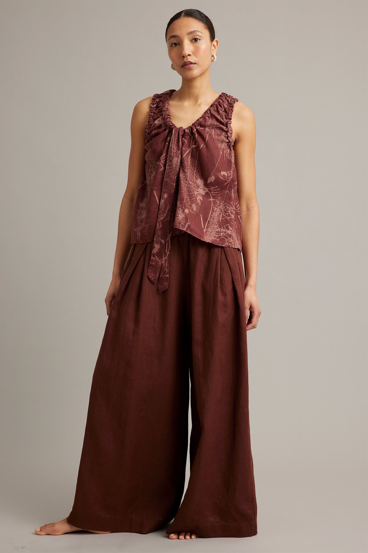 Edestäpäin: Nainen viininpunaisissa leveälahkeisissa pellavahousuissa ja kuviollisessa hihattossa topissa.