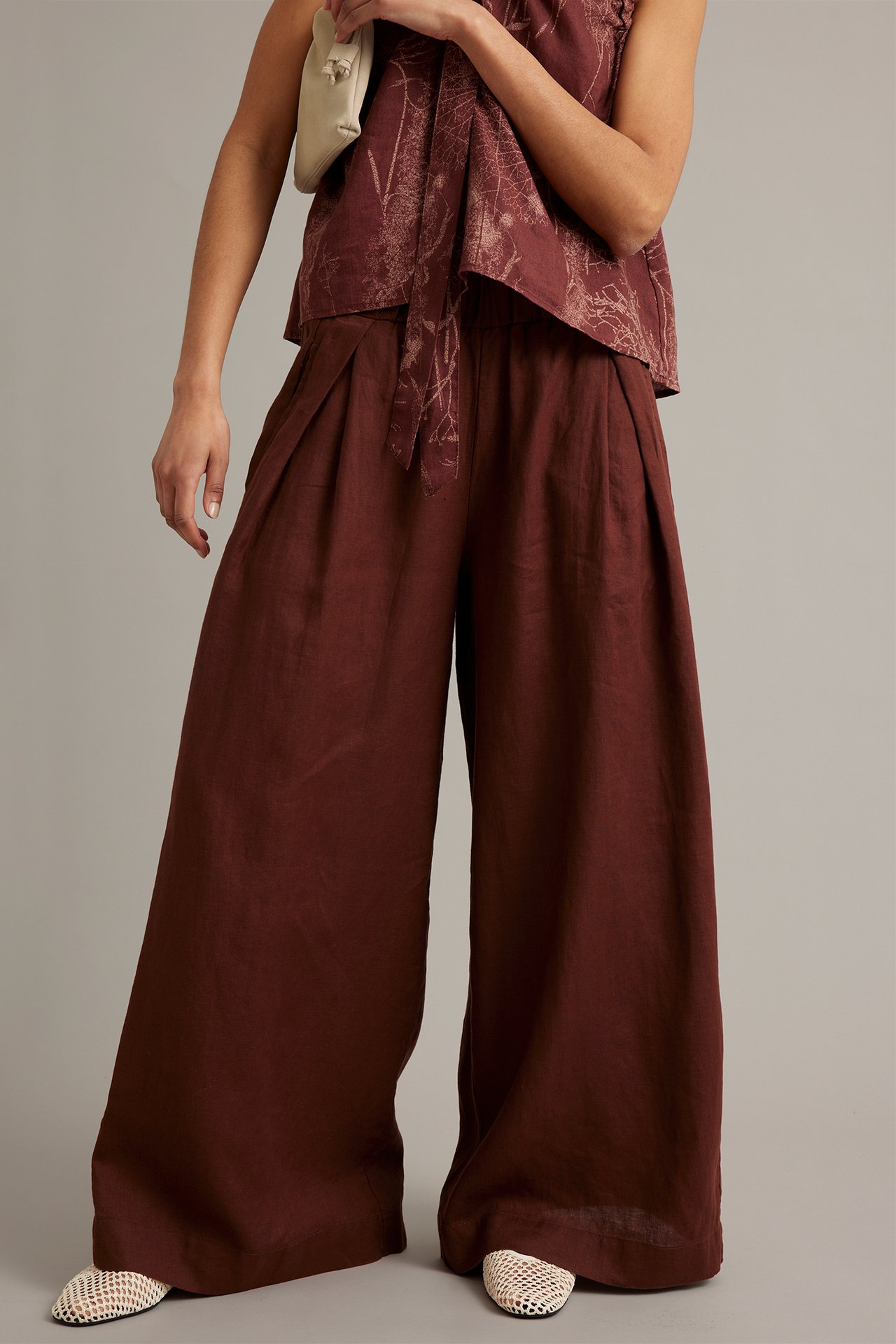 Kvinne i vinrøde vide linbukser med legg, mønstret topp og lyse nettingballerinas, sett forfra.