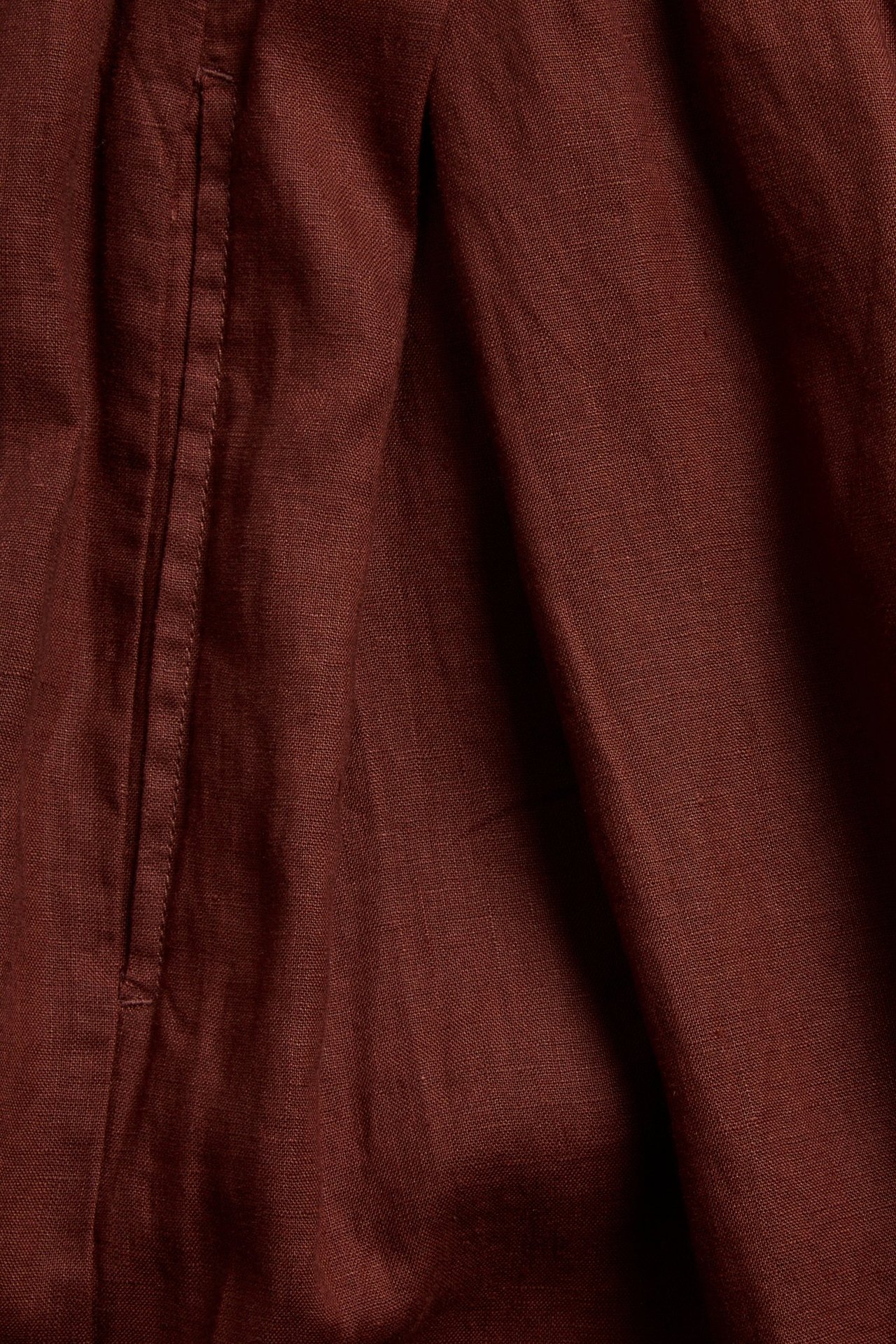 Lähikuva viininpunaisista pellavahousuista, näyttää sivutaskun, laskoksen ja kankaan tekstuurin.