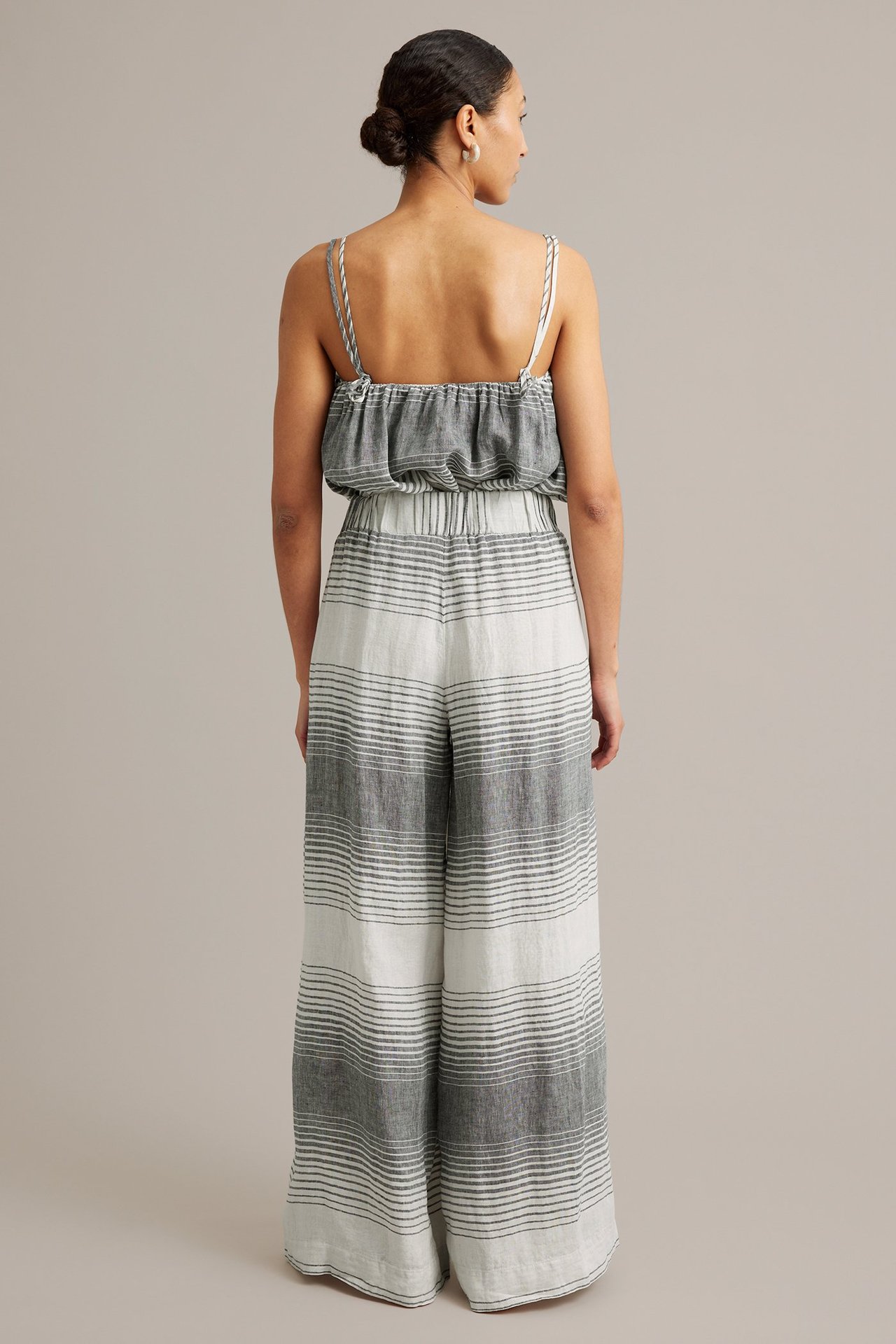 Kvinna sedd bakifrån i vida mörkgrå- och vitrandiga linnebyxor med matchande linne.