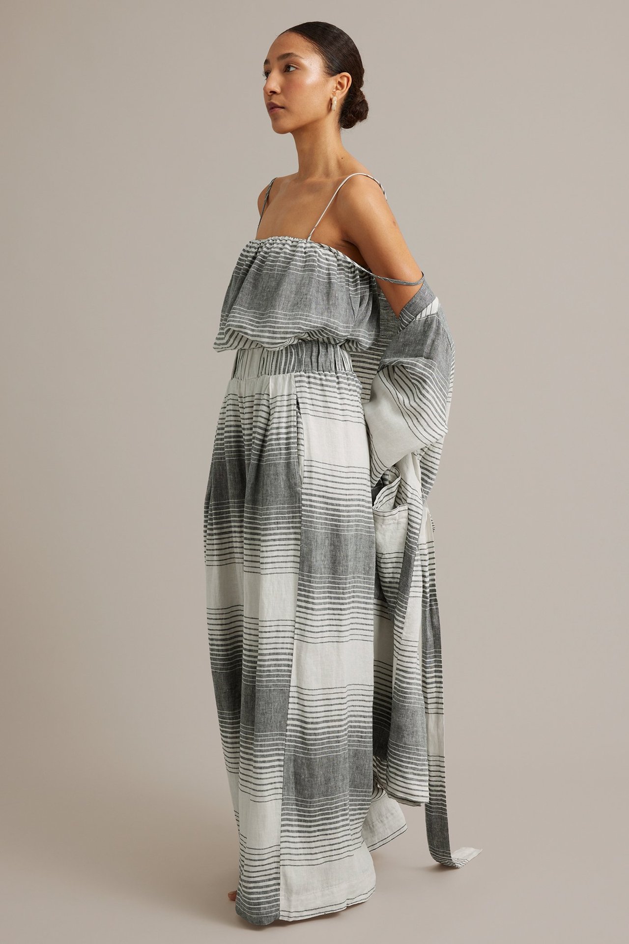 Sidovy: Kvinna i mörkgrå och vitrandiga vida linnebyxor, matchande topp och öppen lång skjorta.