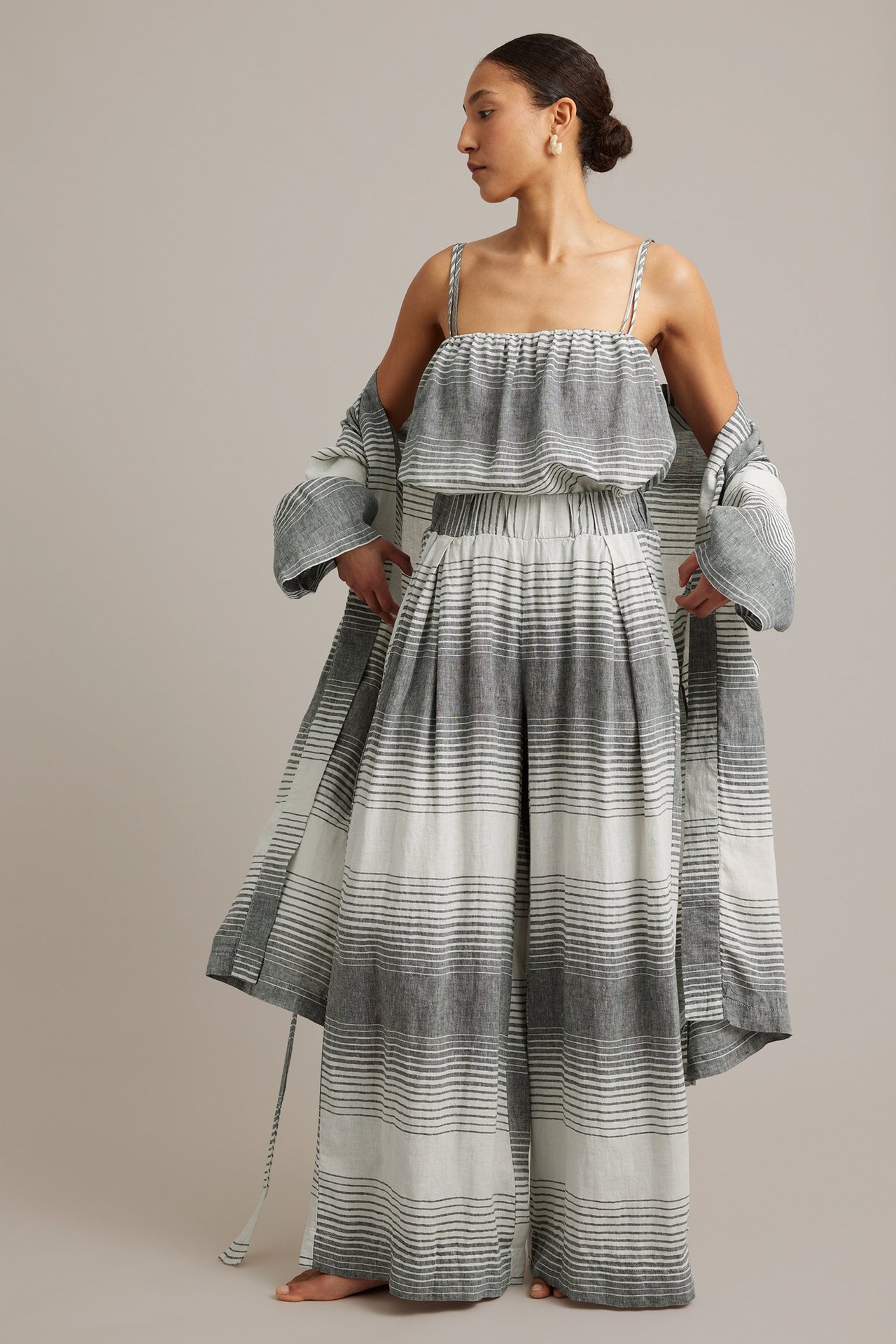 Framifrån, kvinna i randiga mörkblå vida linnebyxor, matchande topp och öppen lång rock.