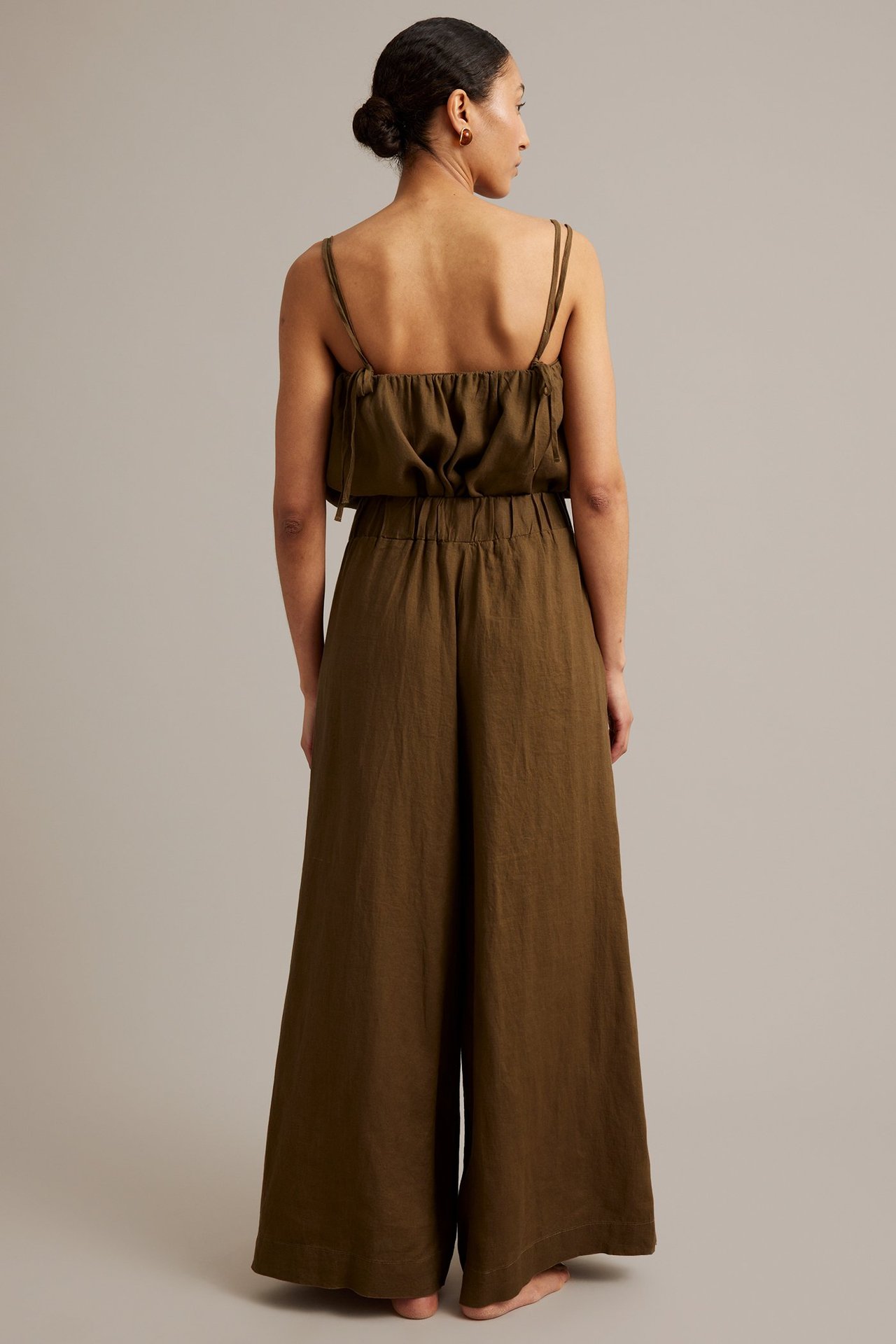 Ryggbild av en kvinna i bruna vida linnebyxor med resår i midjan och matchande brun linne-cami.