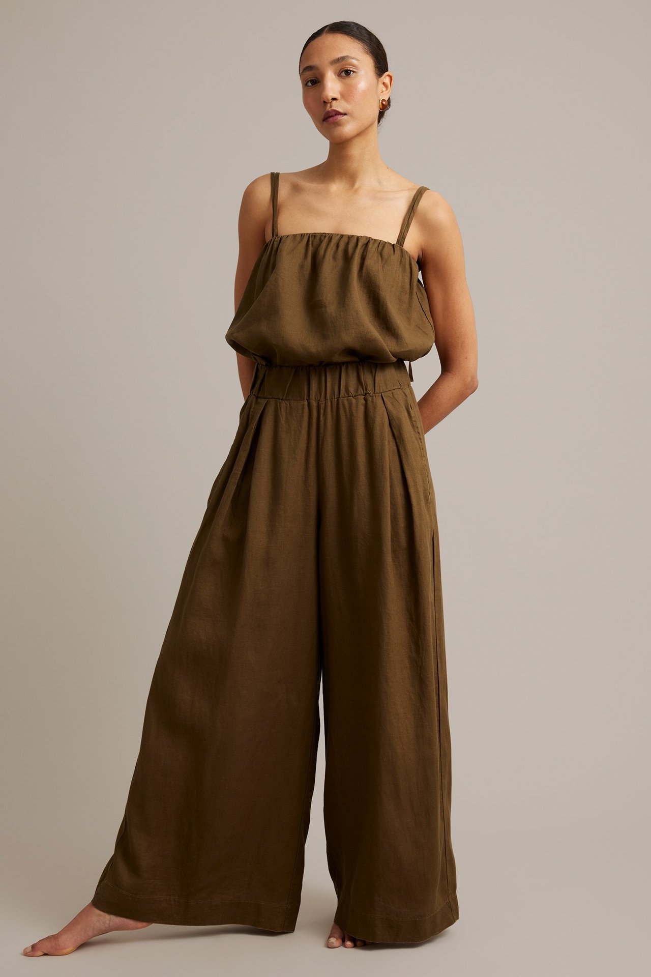 Frontvy av kvinna i bruna vida linnebyxor med veck och matchande camisoletopp.