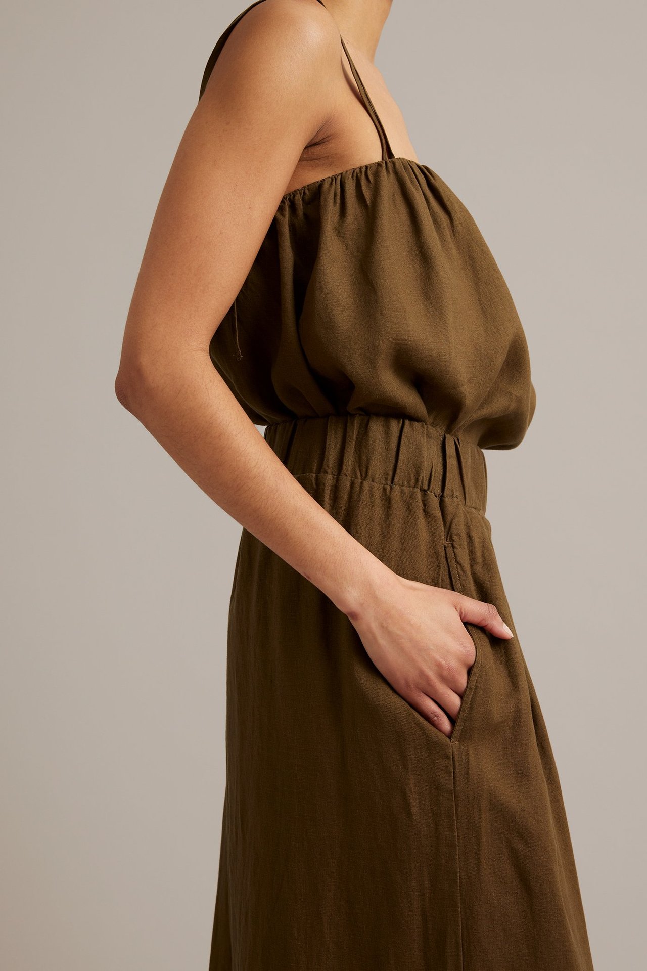 Sidovy av kvinna i bruna linnebyxor med vid passform, resår i midjan och sidfickor.