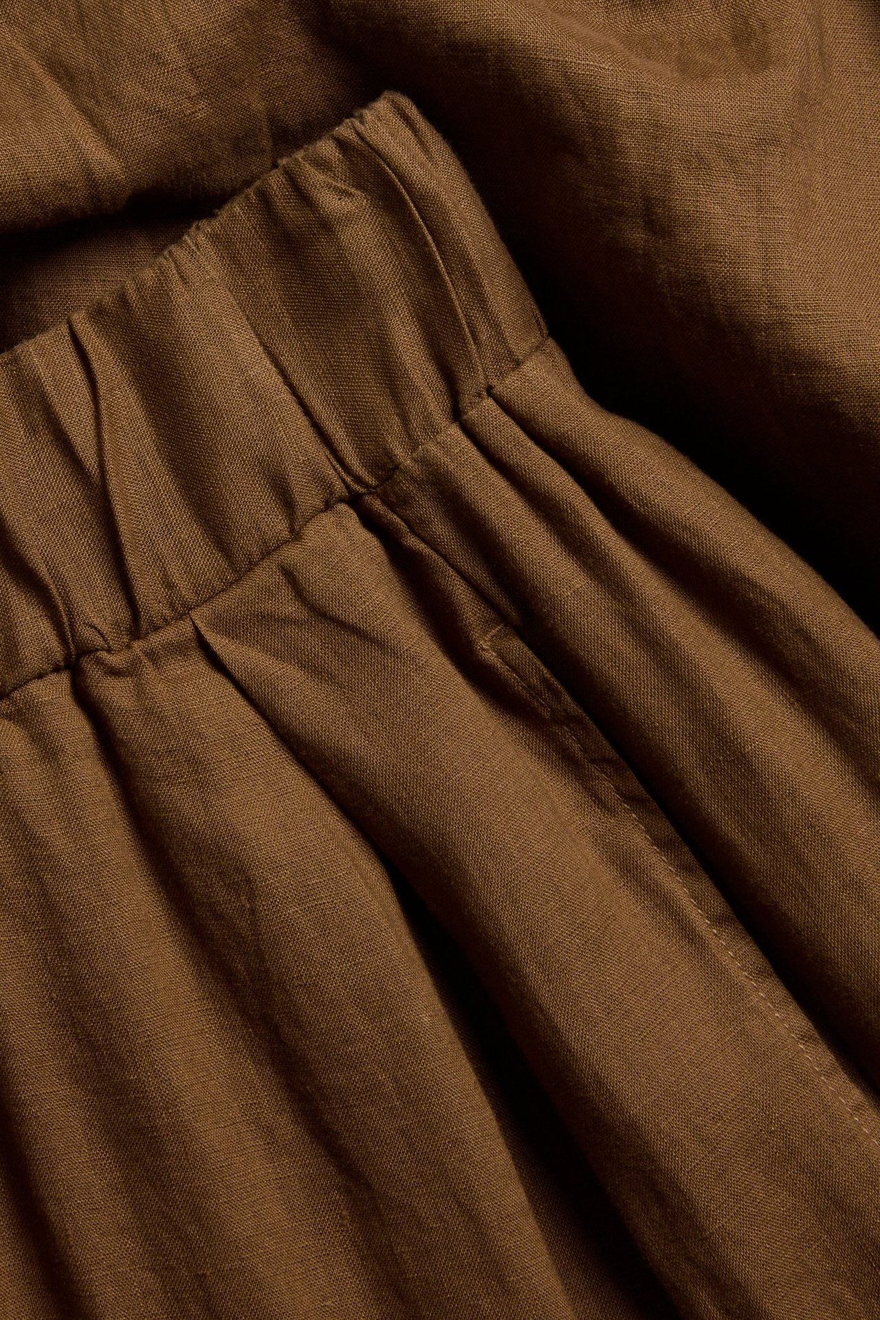 Zbliżenie na brązowe lniane spodnie wide fit z elastyczną talią, zaszewkami i bocznymi kieszeniami.