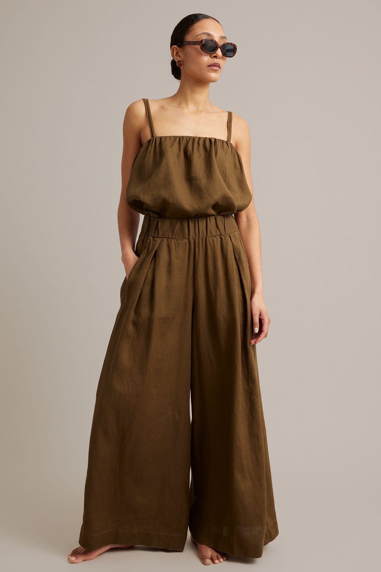 Helkroppsvy: Kvinne i brune vide linbukser med legg, elastisk midje, matchende topp og solbriller.