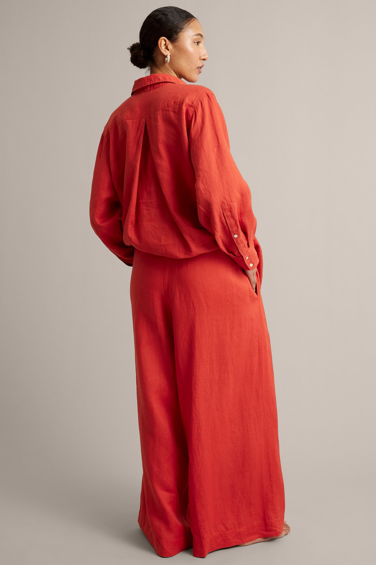 Side-bakfra visning av kvinne i røde vide linbukser med matchende rød linskjorte og øreringer.