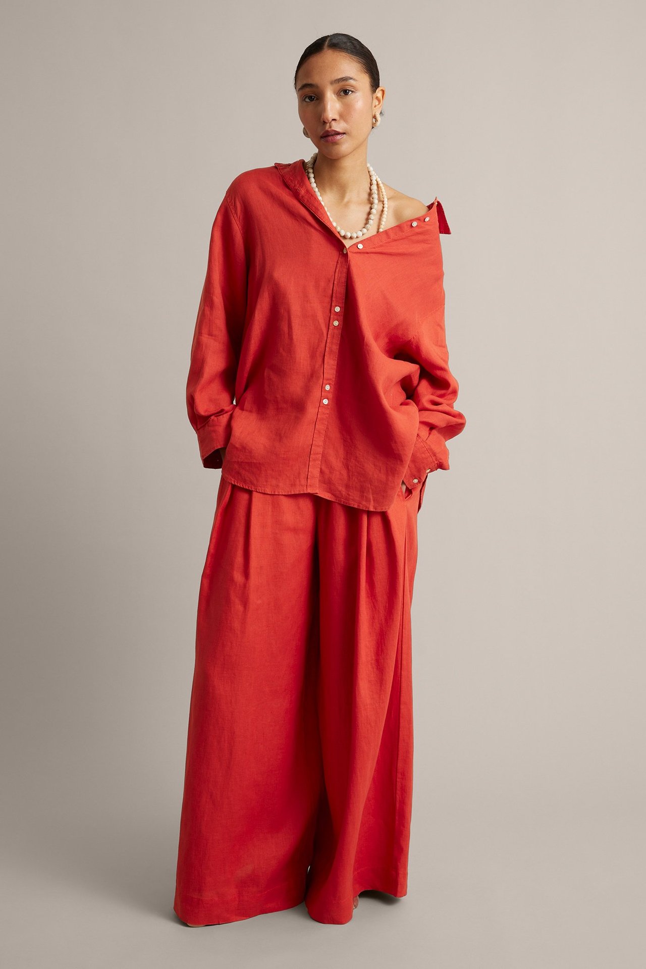 Frontbilde: Kvinne i røde vide lnbukser, matchende linskjorte, perlekjede og øreringer.