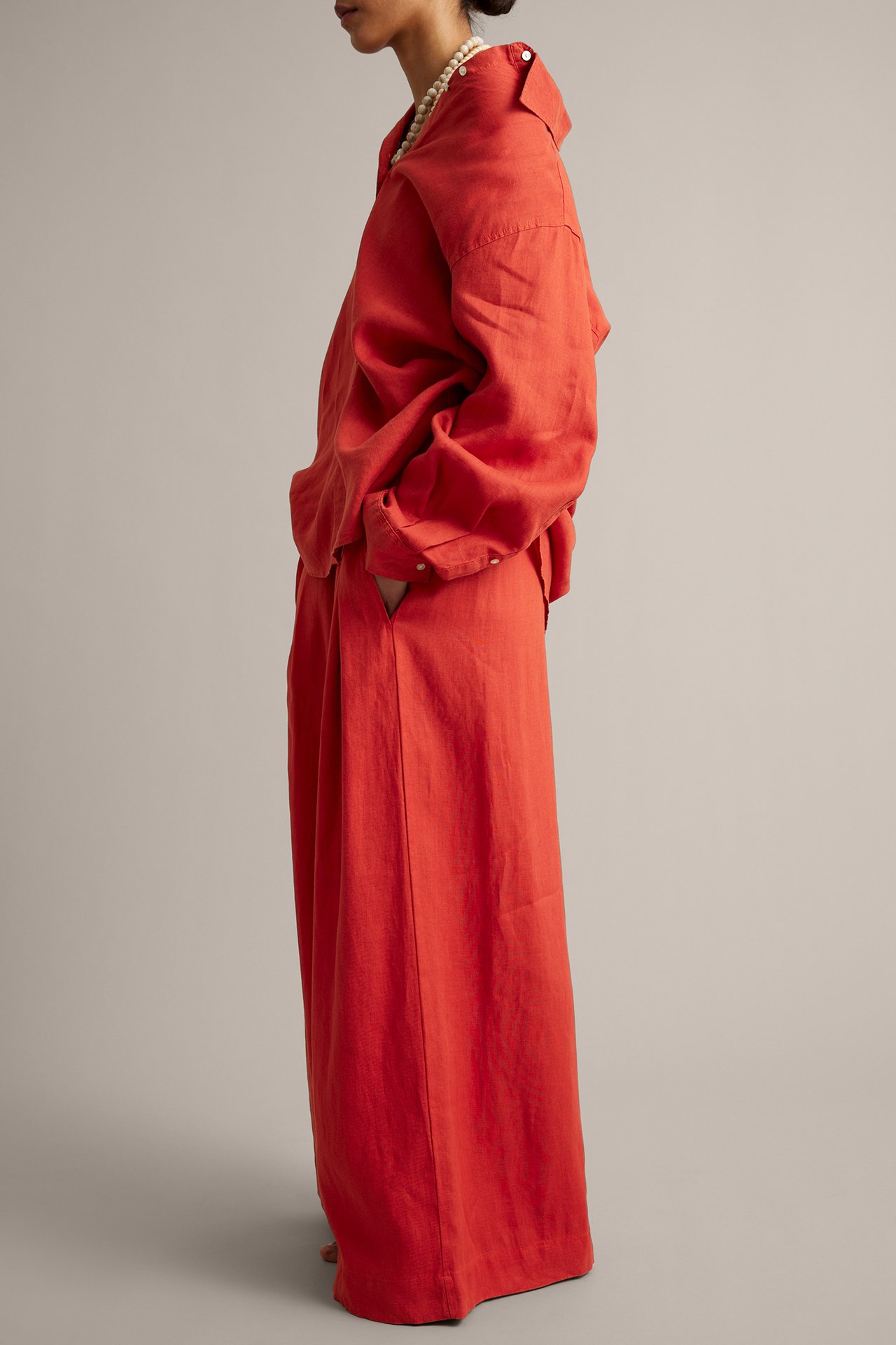 Sidebilde av en kvinne i røde vide linbukser, en matchende skjorte og et perlekjede.